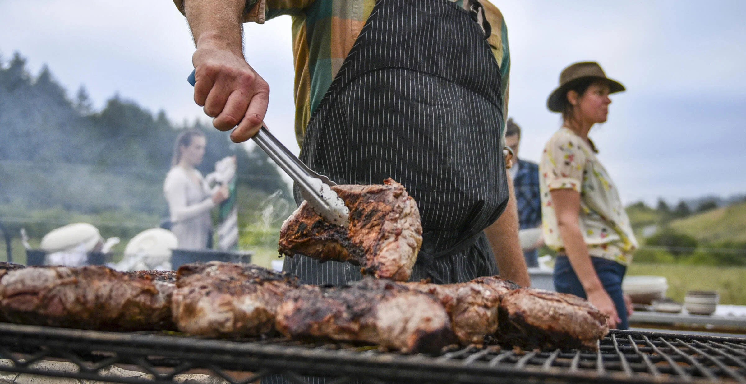A man flips a steak with tongs at a barbecue grill. 