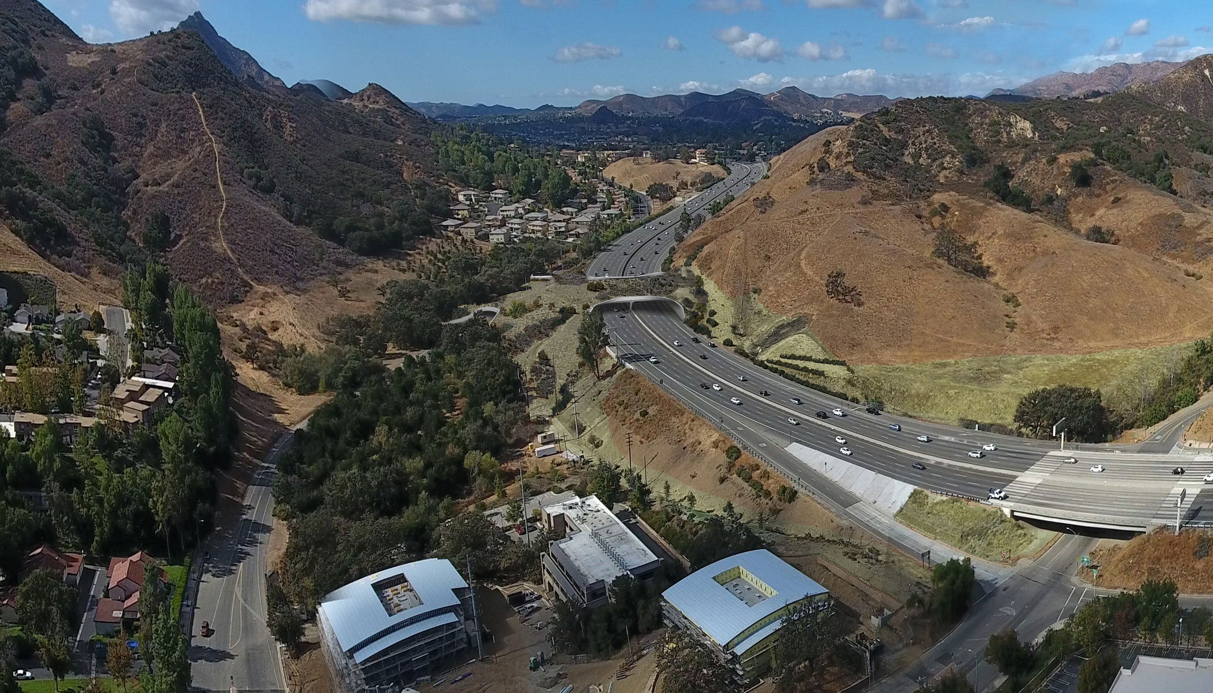 Image composite of an overpass stretching over a 10-lane highway in a mountainous landscape.