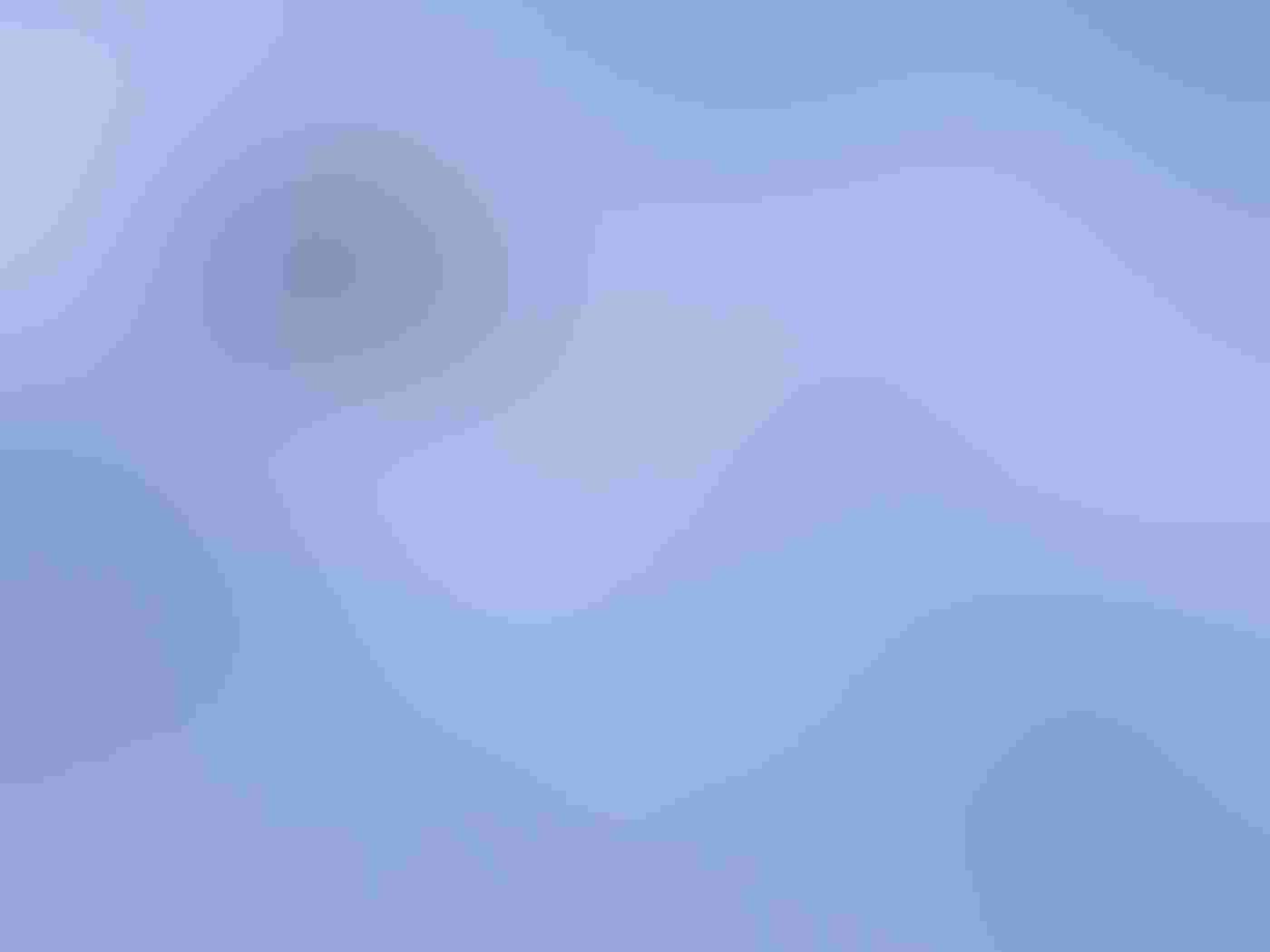 A Gentoo Penguin leans into the sea. The bird is surrounded by soft blue blurred water coming from several directions. The penguin is in sharp focus, its black and white coloring standing out from the blue surf.