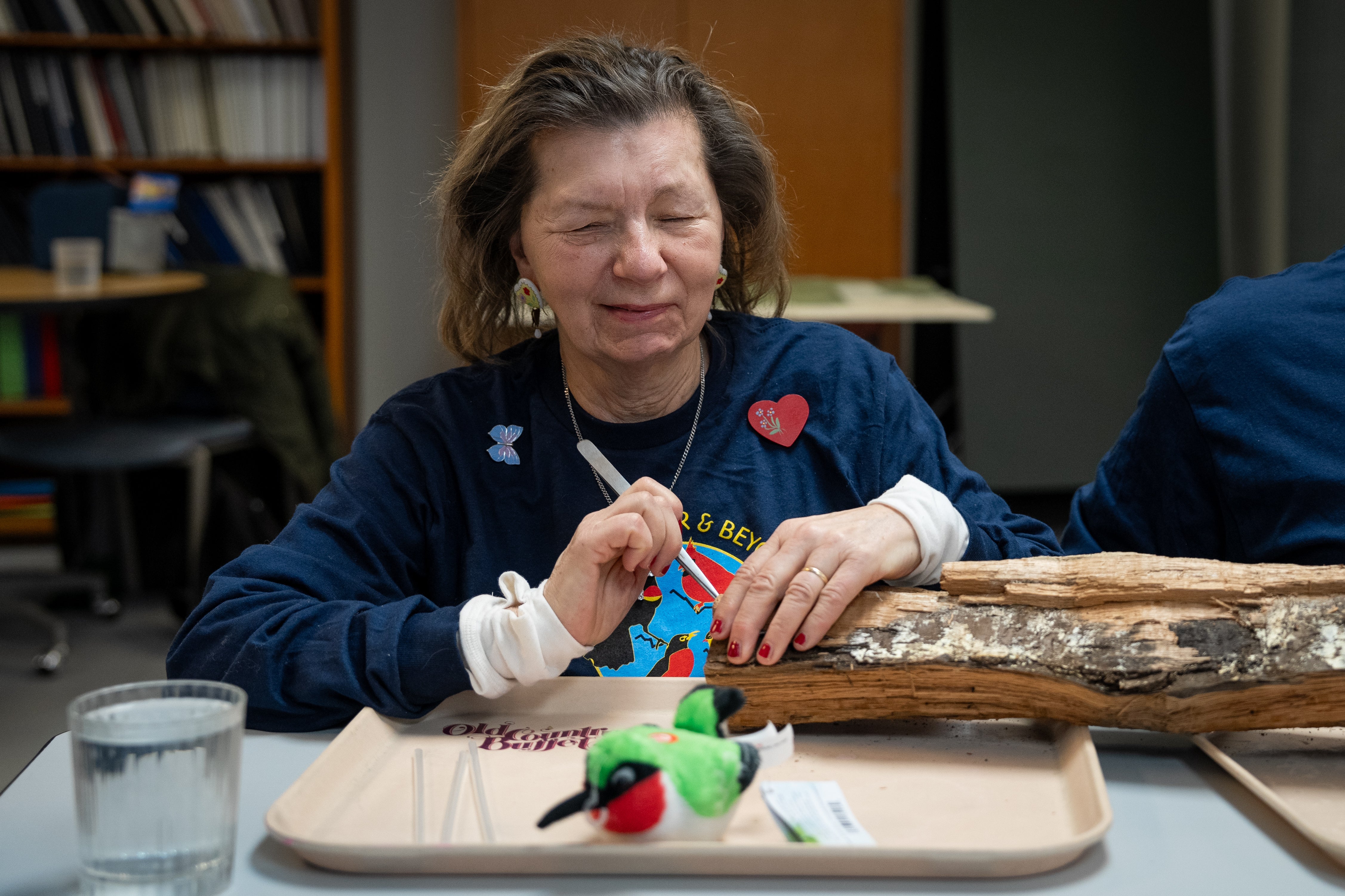 Donna Posont sits at a table holding tweezers with a log in front of her.