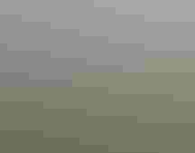 Two people stand next to a truck in a hilly landscape, flying a drone over a landing pad.