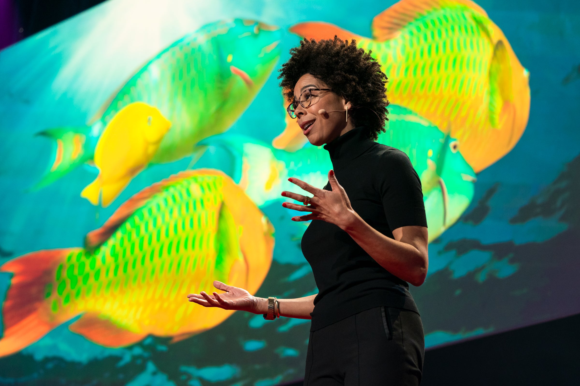 Ayana Johnson on a stage in front of a video wall featuring colorful fish and coral. 