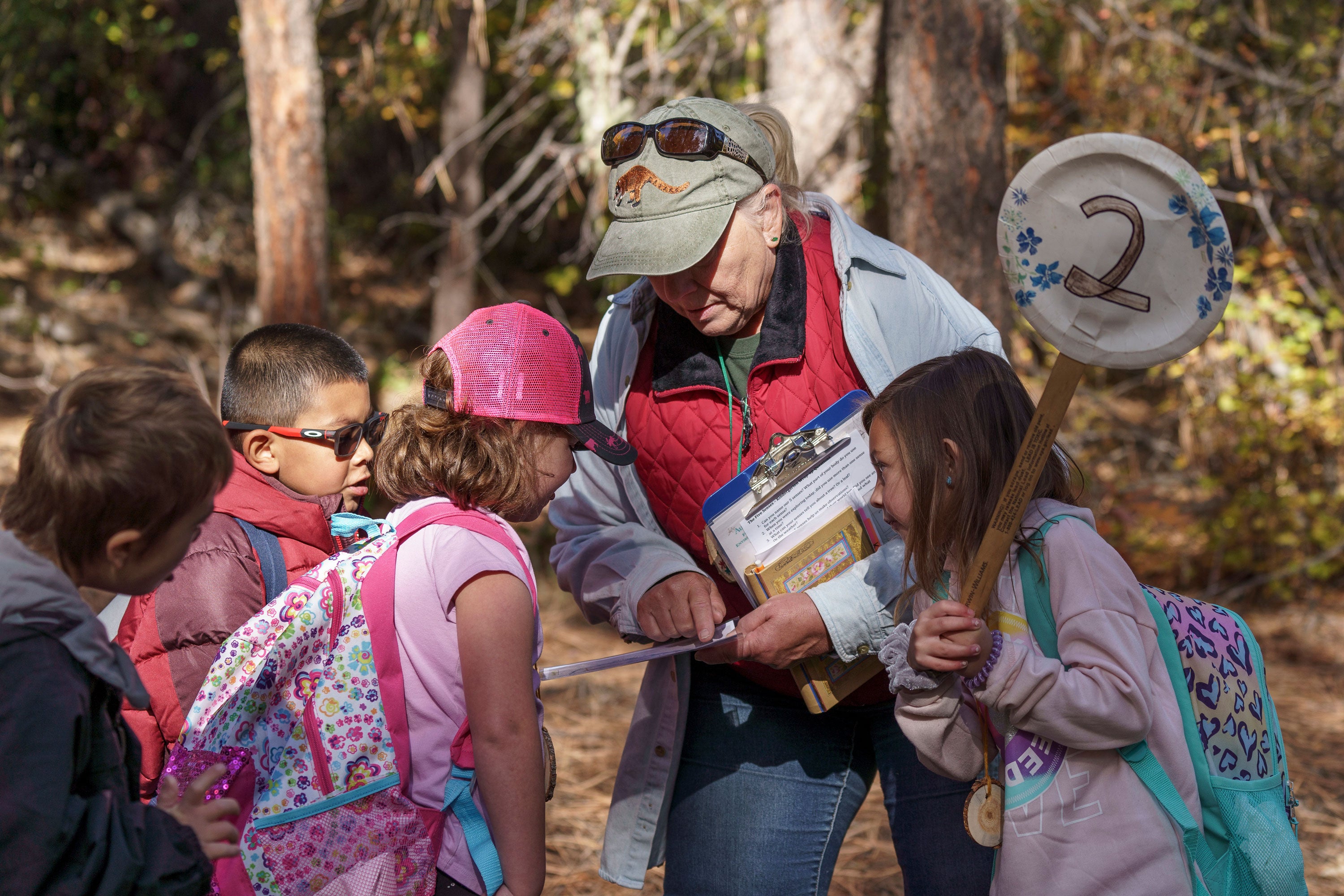 A woman and children look at a paper in a forest.