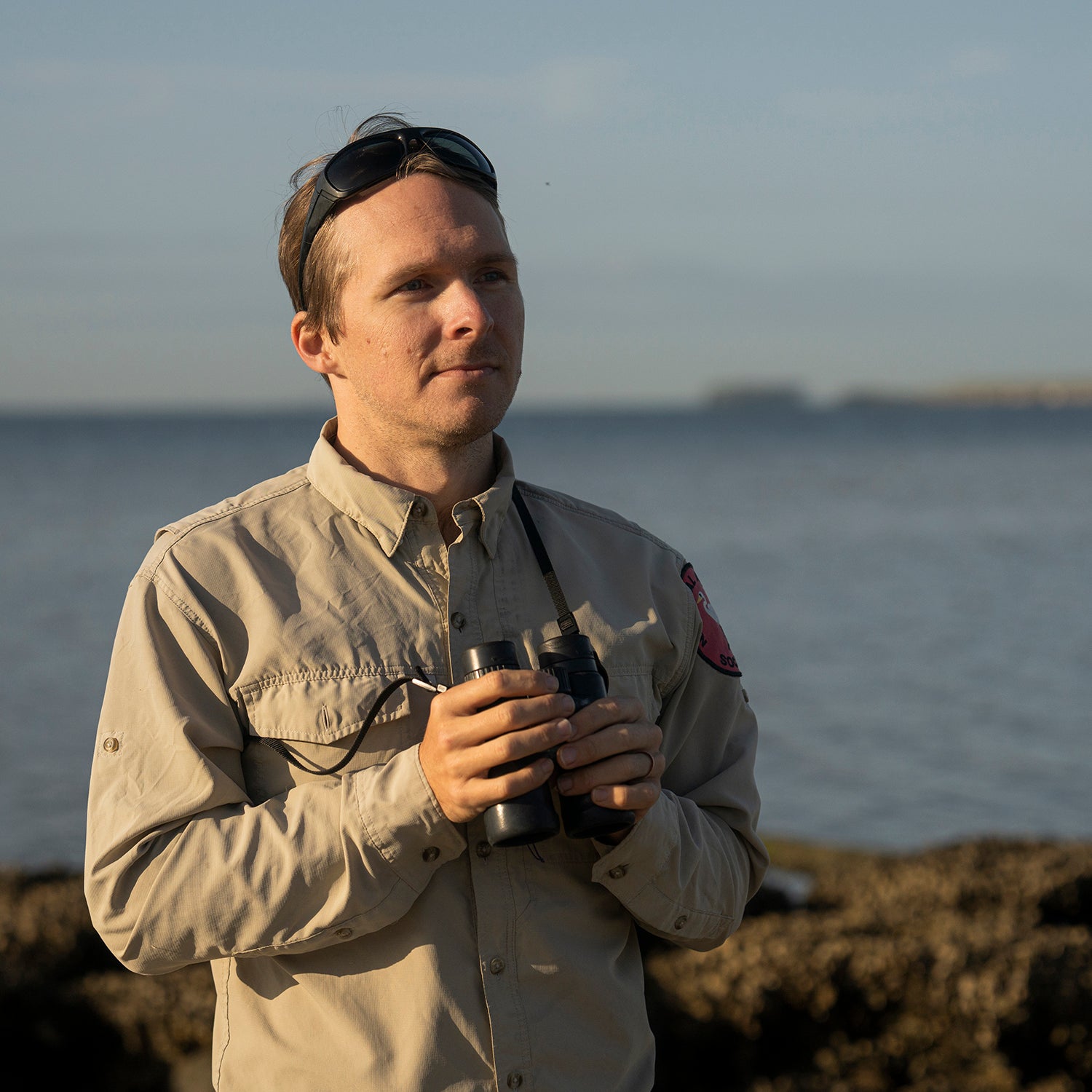 A man holding binoculars on a rocky jetty