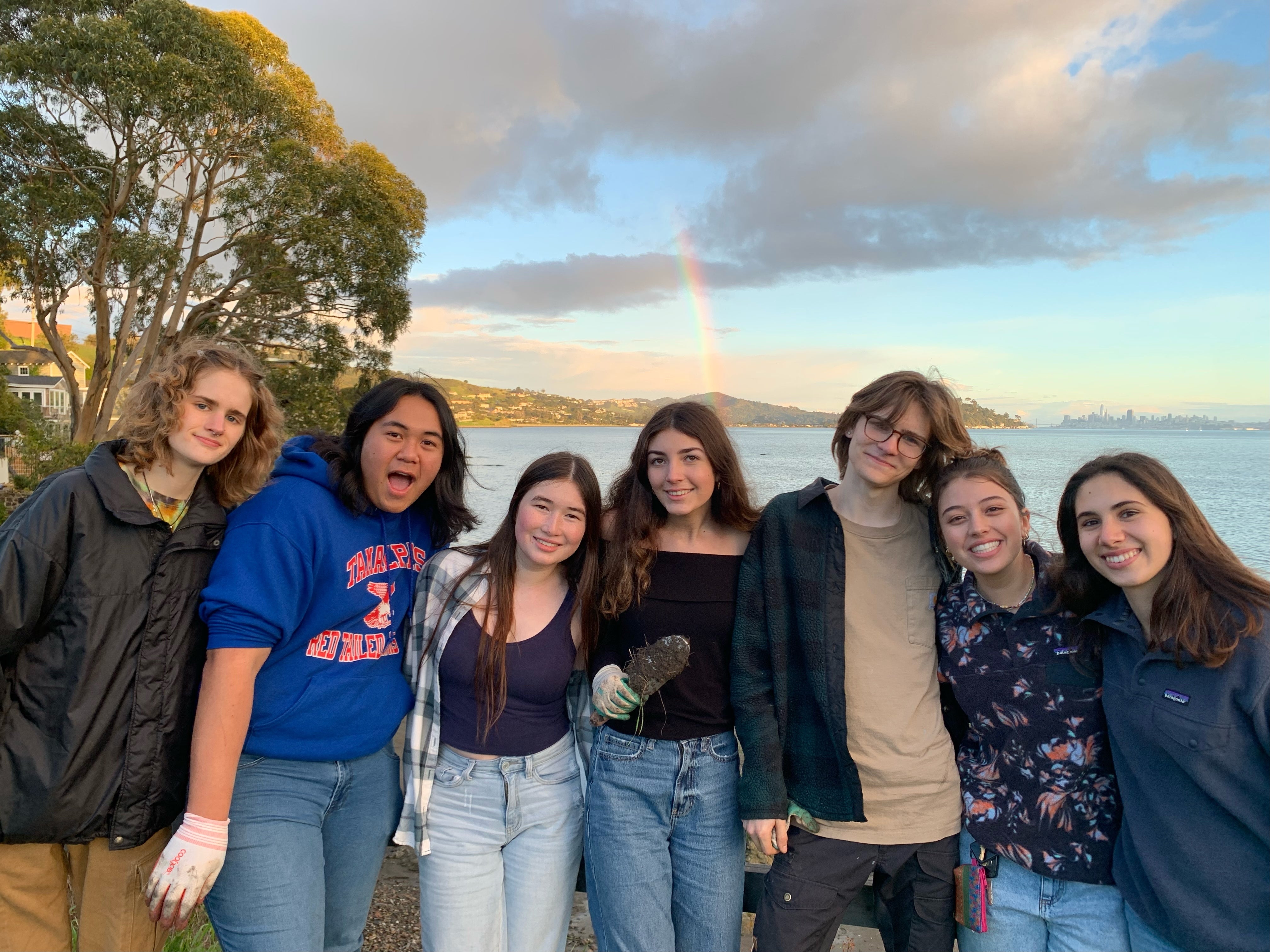 Group of smiling young people look at the camera while a rainbow arcs in the background