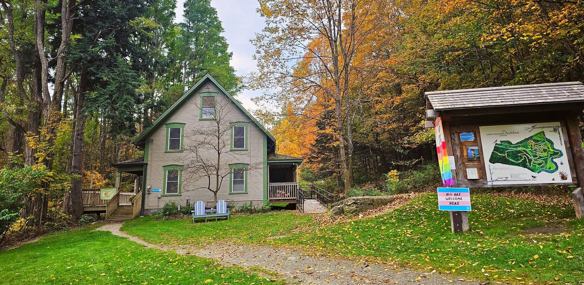 A building with brown siding, green windows, and a Pride Flag hanging outside.