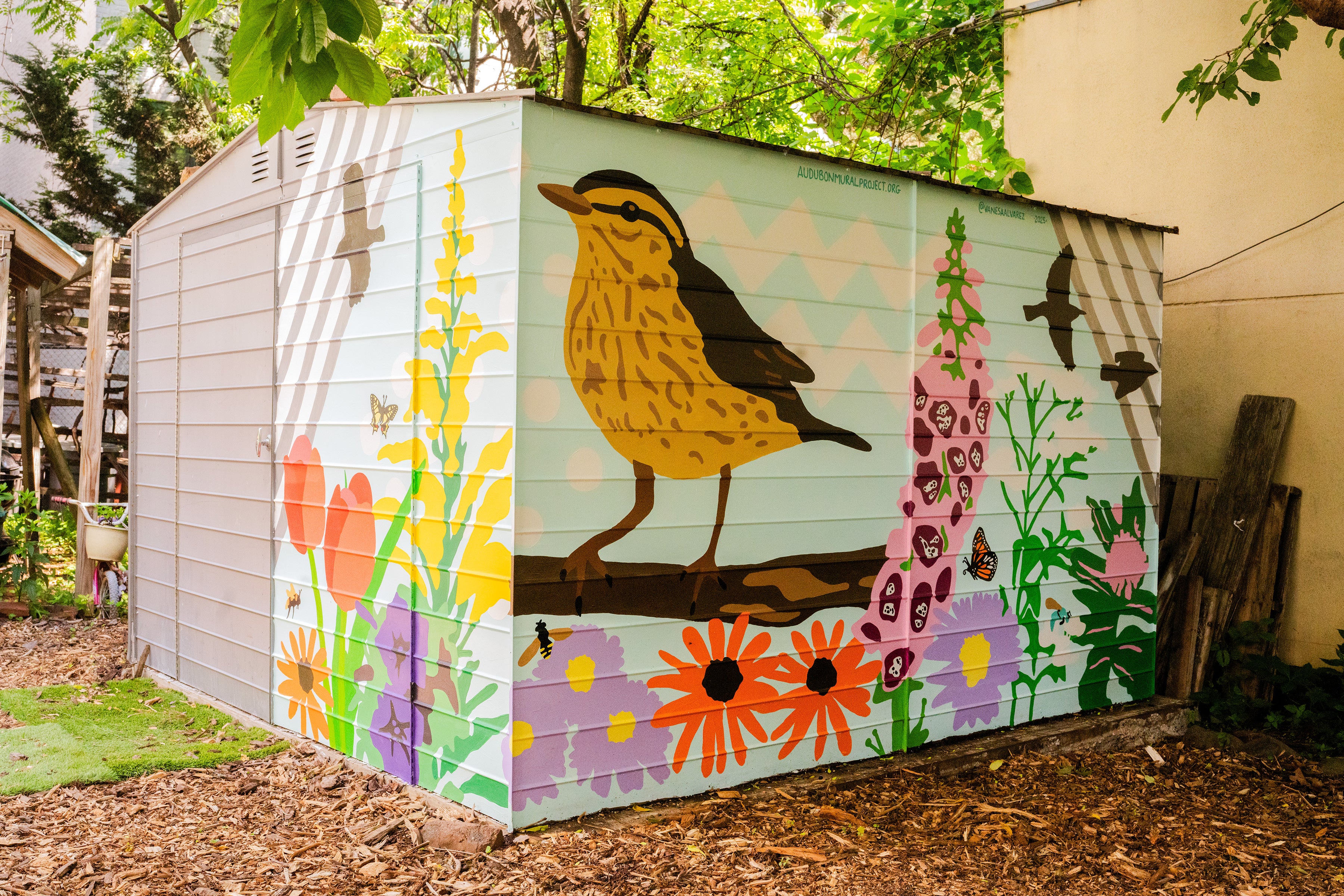 A colorful mural of birds and flowers painted on a garden shed.
