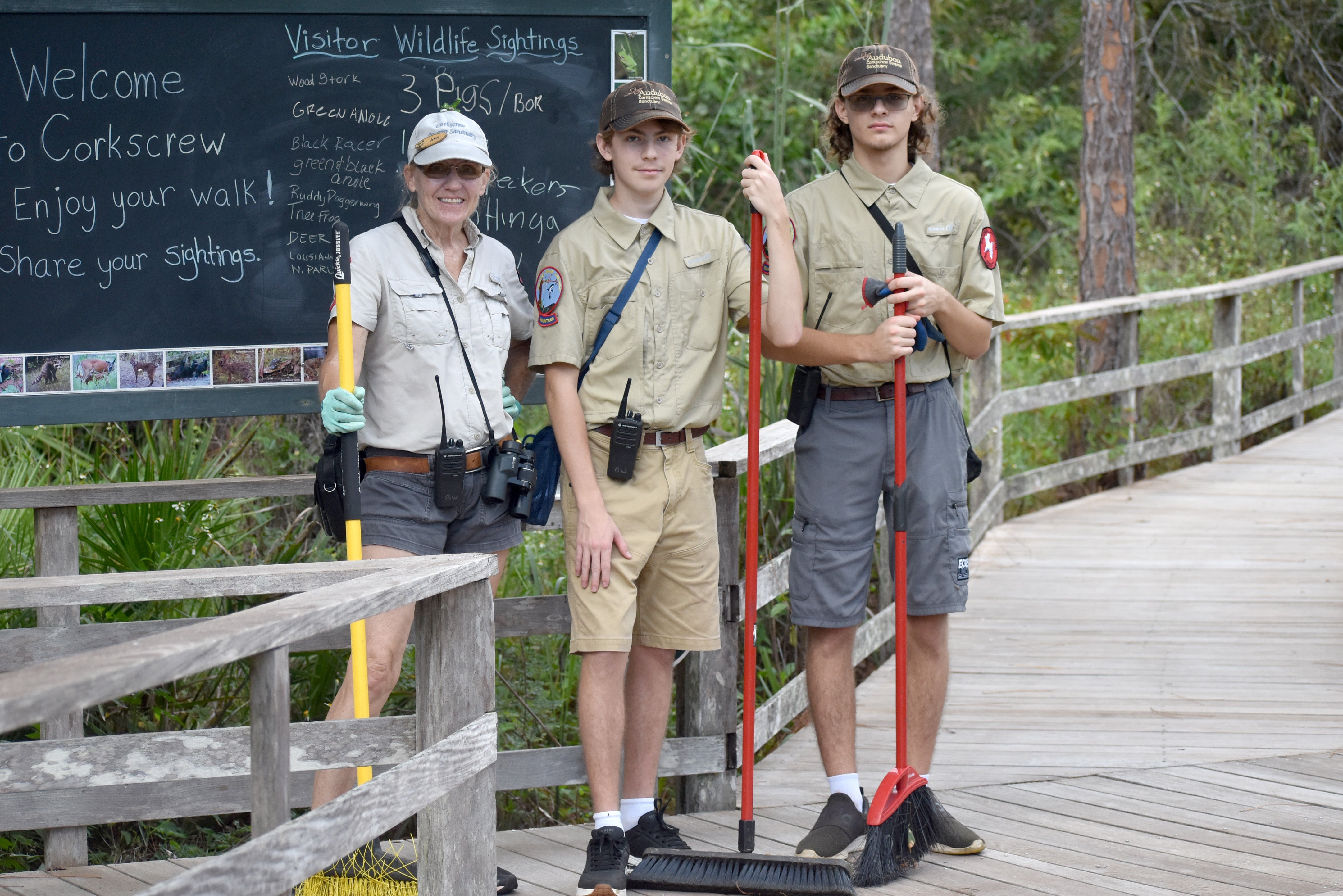 Three people with brooms on a boardwalk