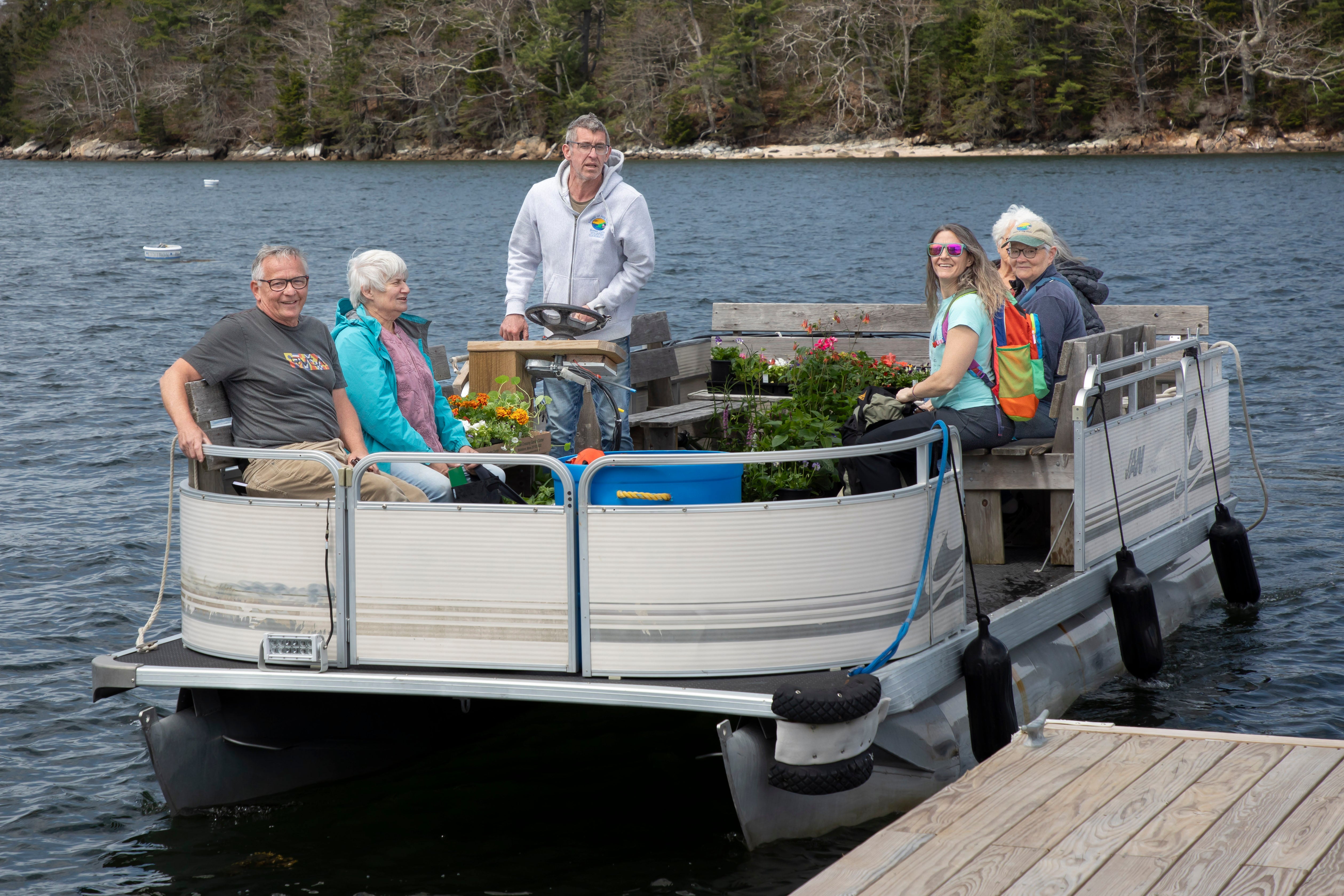 A pontoon boat with five people aboard pulls up to a dock.