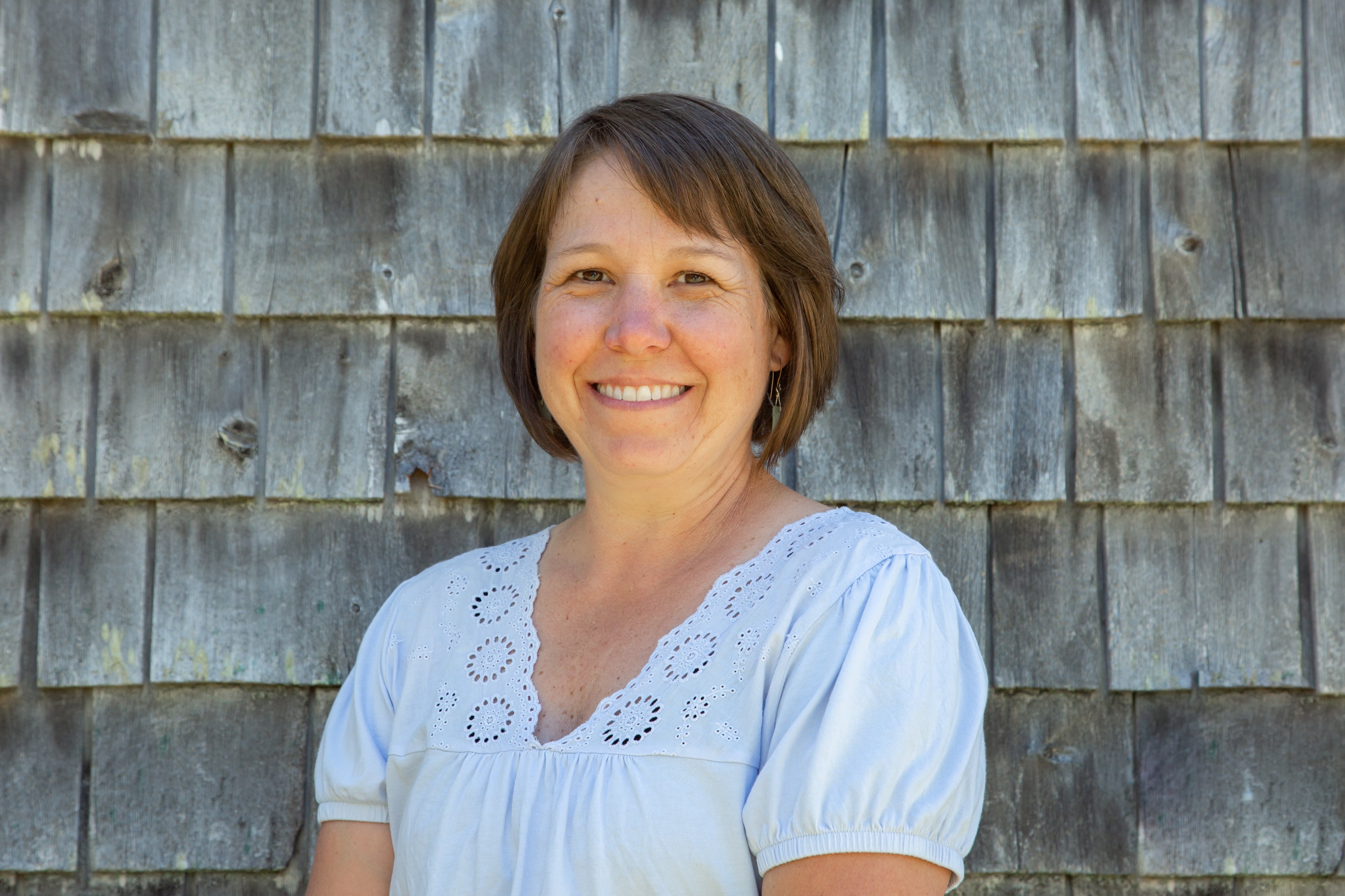 Susie Meadows standing in front of a cedar shingle wall.