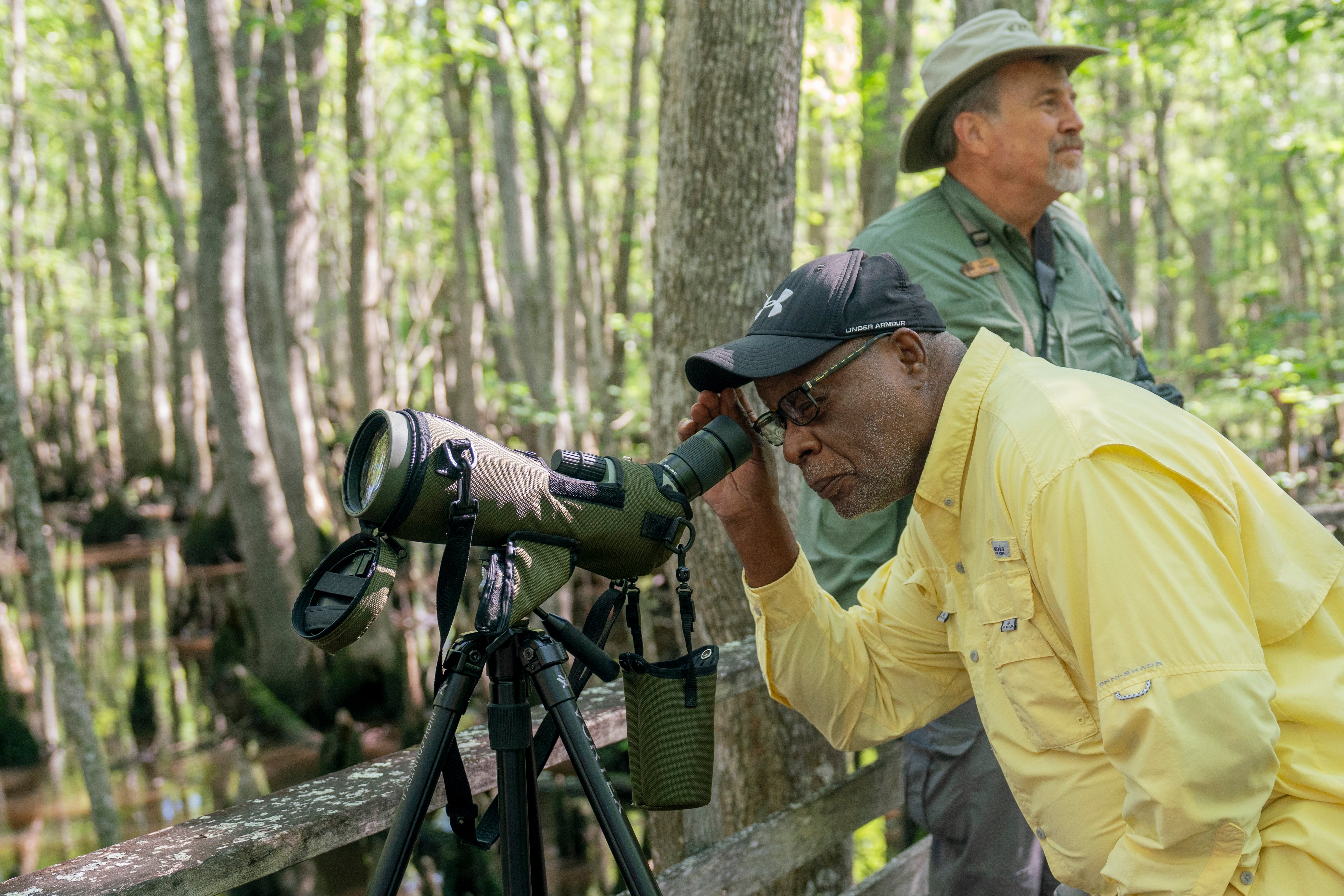 A man looks through a spotting scope in a forest