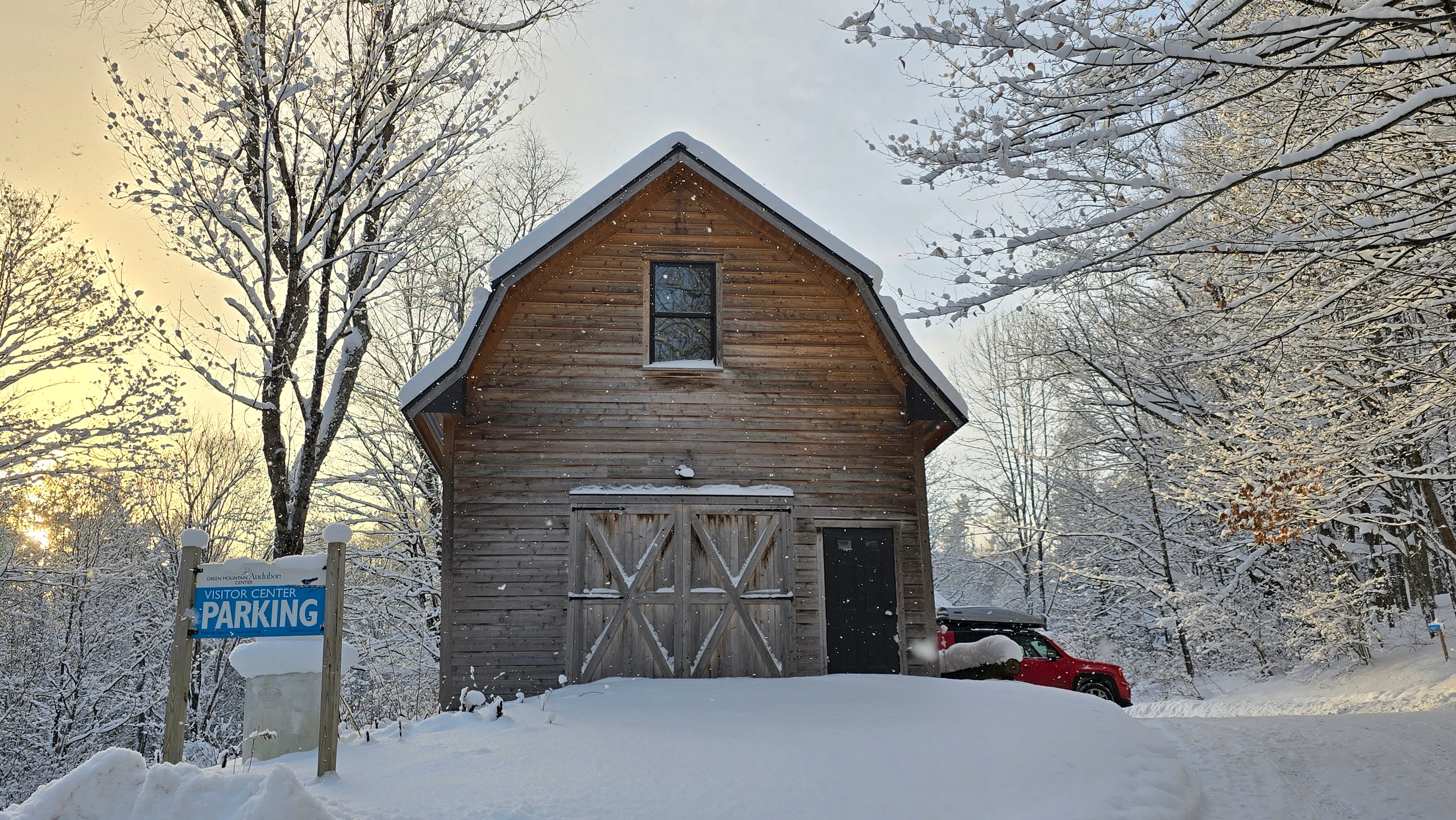A photo of the Education Barn in snow as the sun rises behind it. 