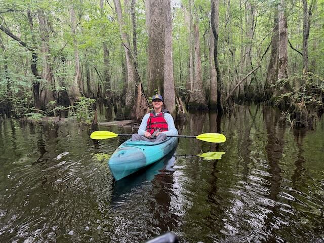 A man sits in a kayak in a dense forest on calm water