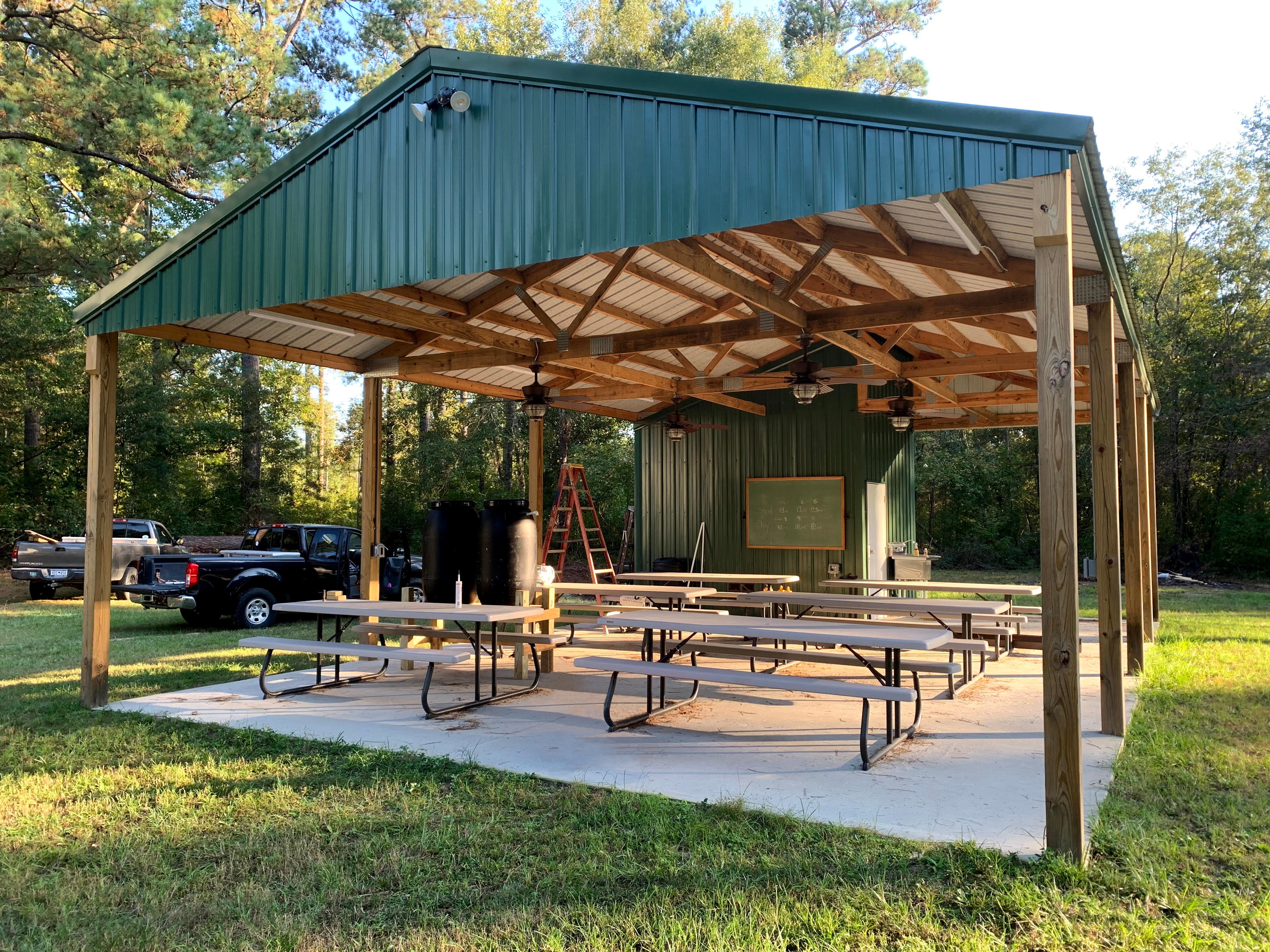 A green roofed pavilion covers a cement slab foundation and picnic tables