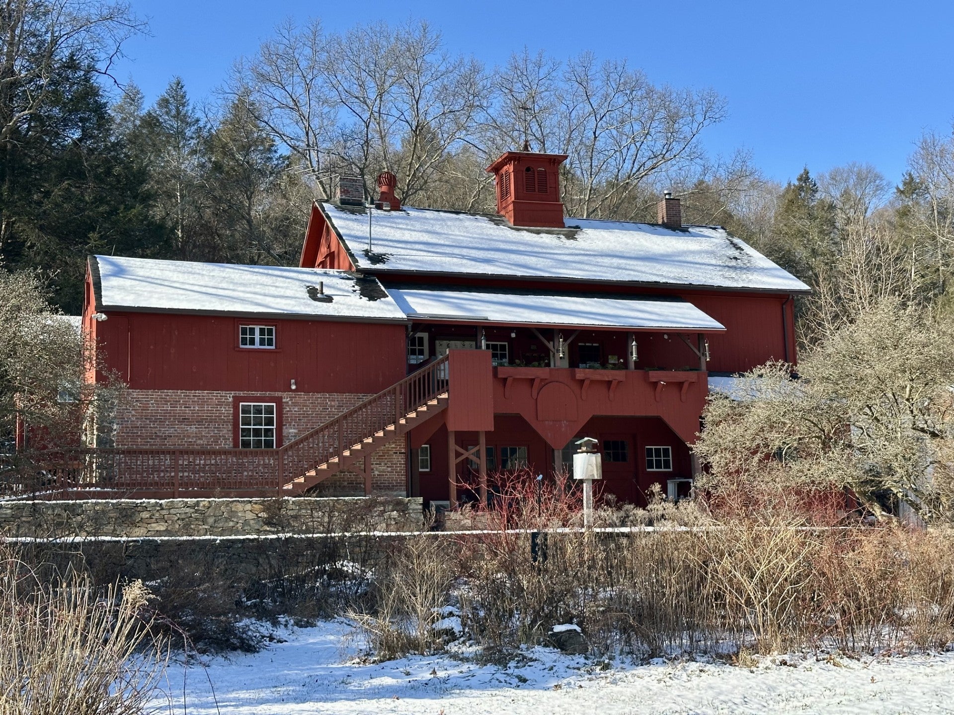 A photo of dark red buildings surrounded by snowy trees and Shrubs