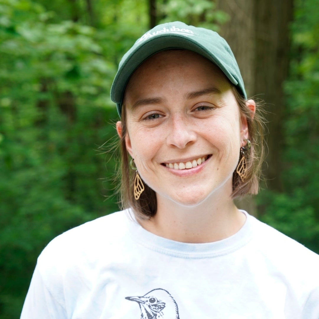 A profile photo of Macie Broussard. She is wearing a shirt with a Hermit Thrush and a green Audubon baseball cap.