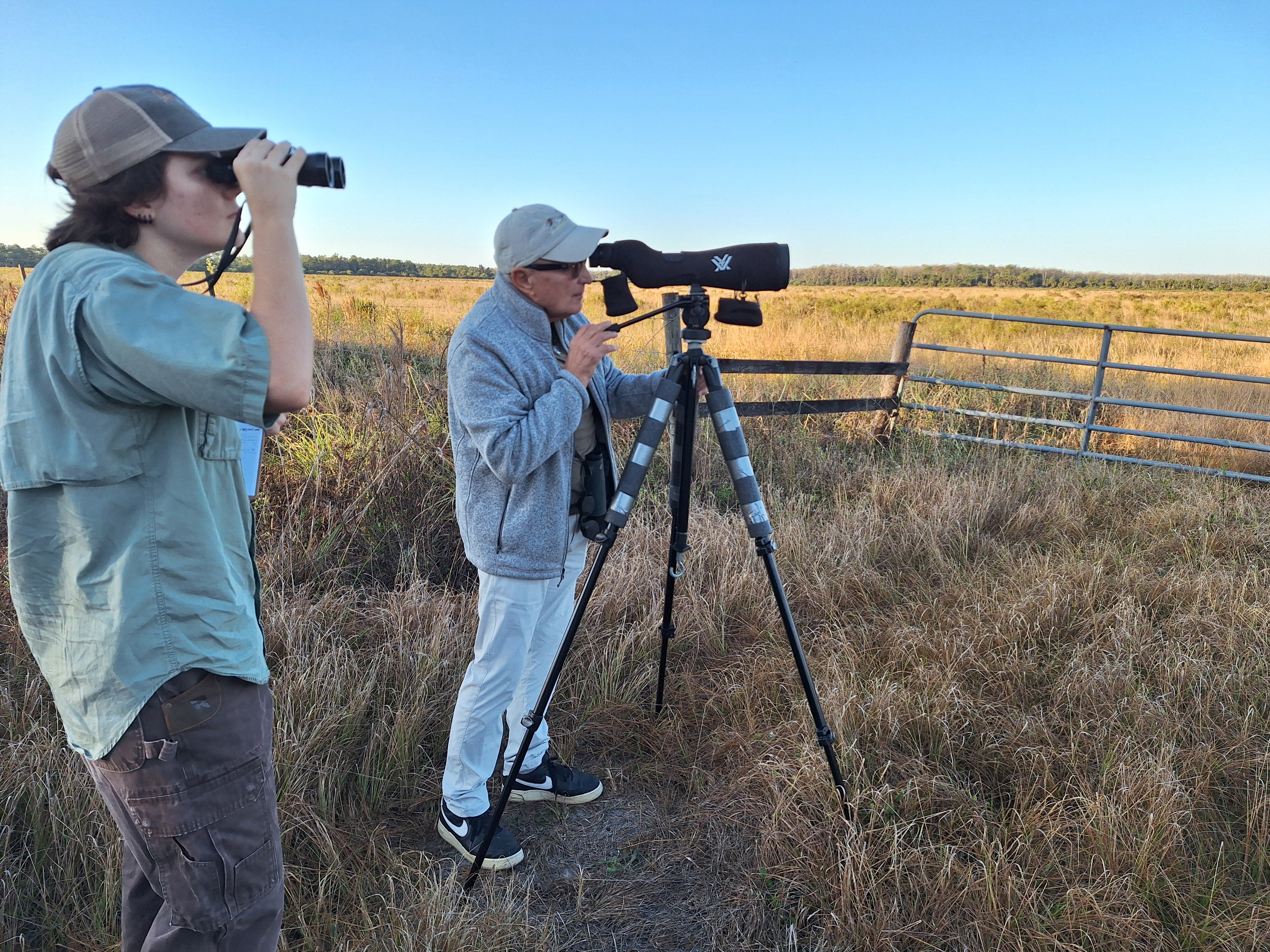Two people with spotting scope and binoculars looking at a field