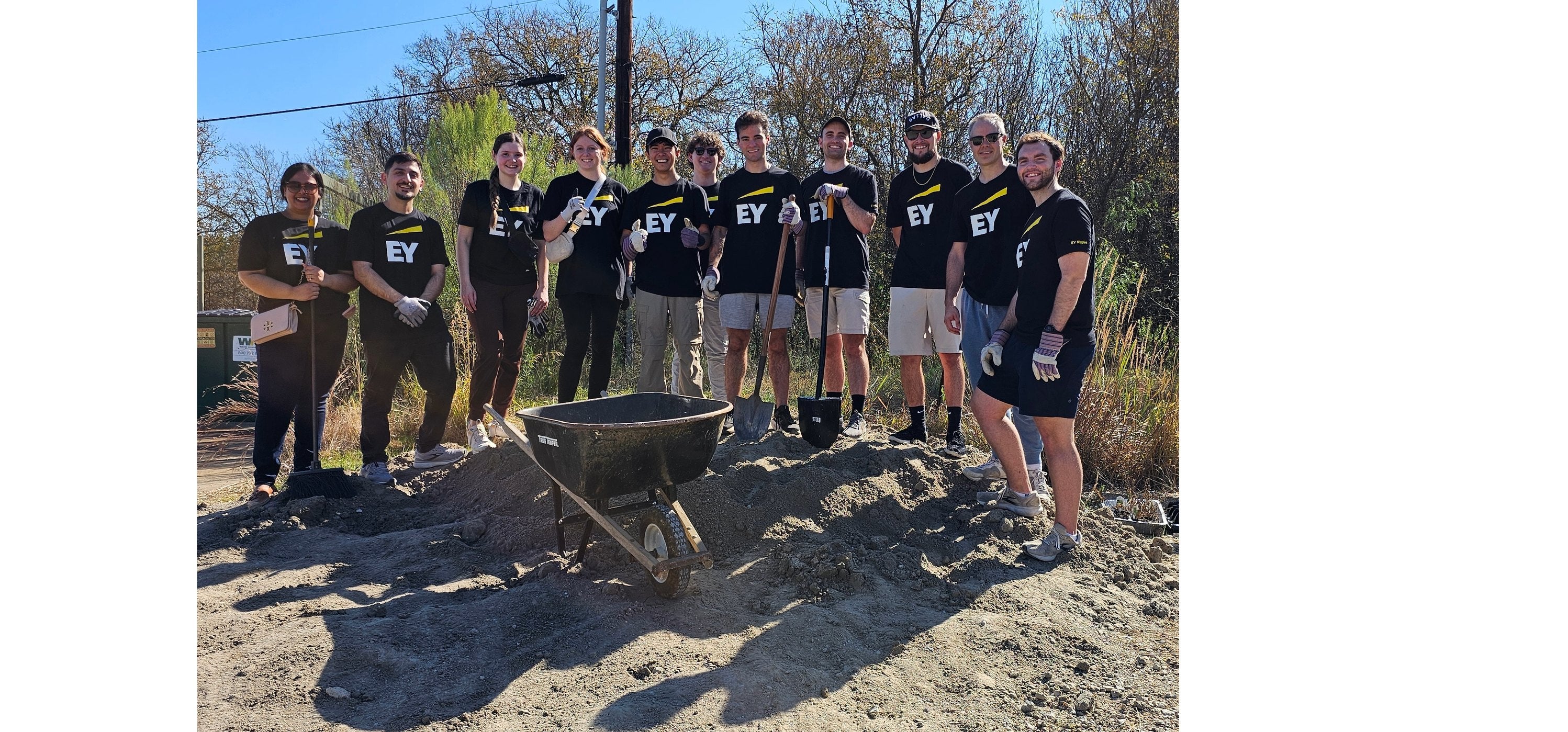 Volunteer group standing on dirt mound with wheelbarrow. 