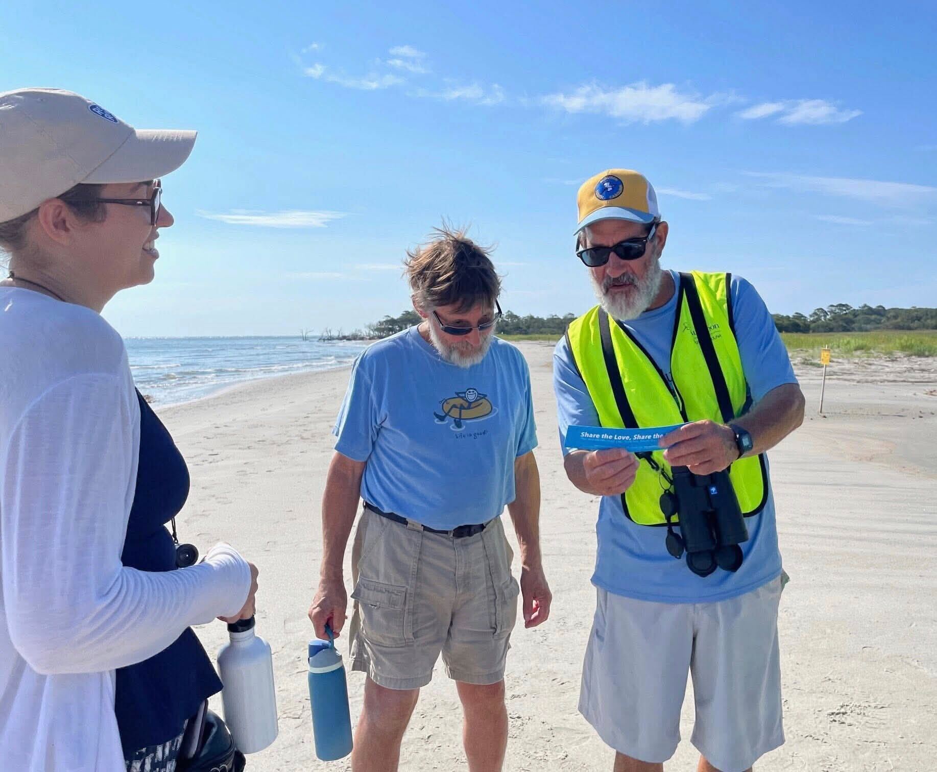 A man in a bright yellow vest shows beach goers some shorebird photos