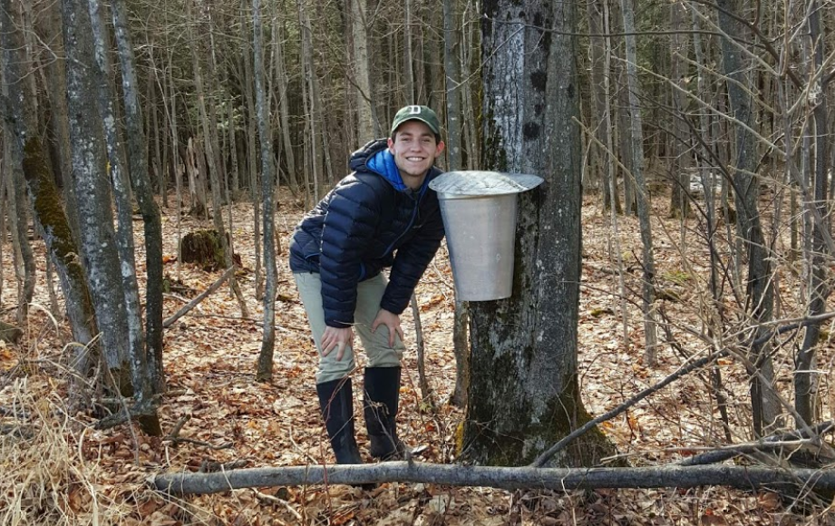 Alexander poses next to a sap bucket on a tree for a photo.