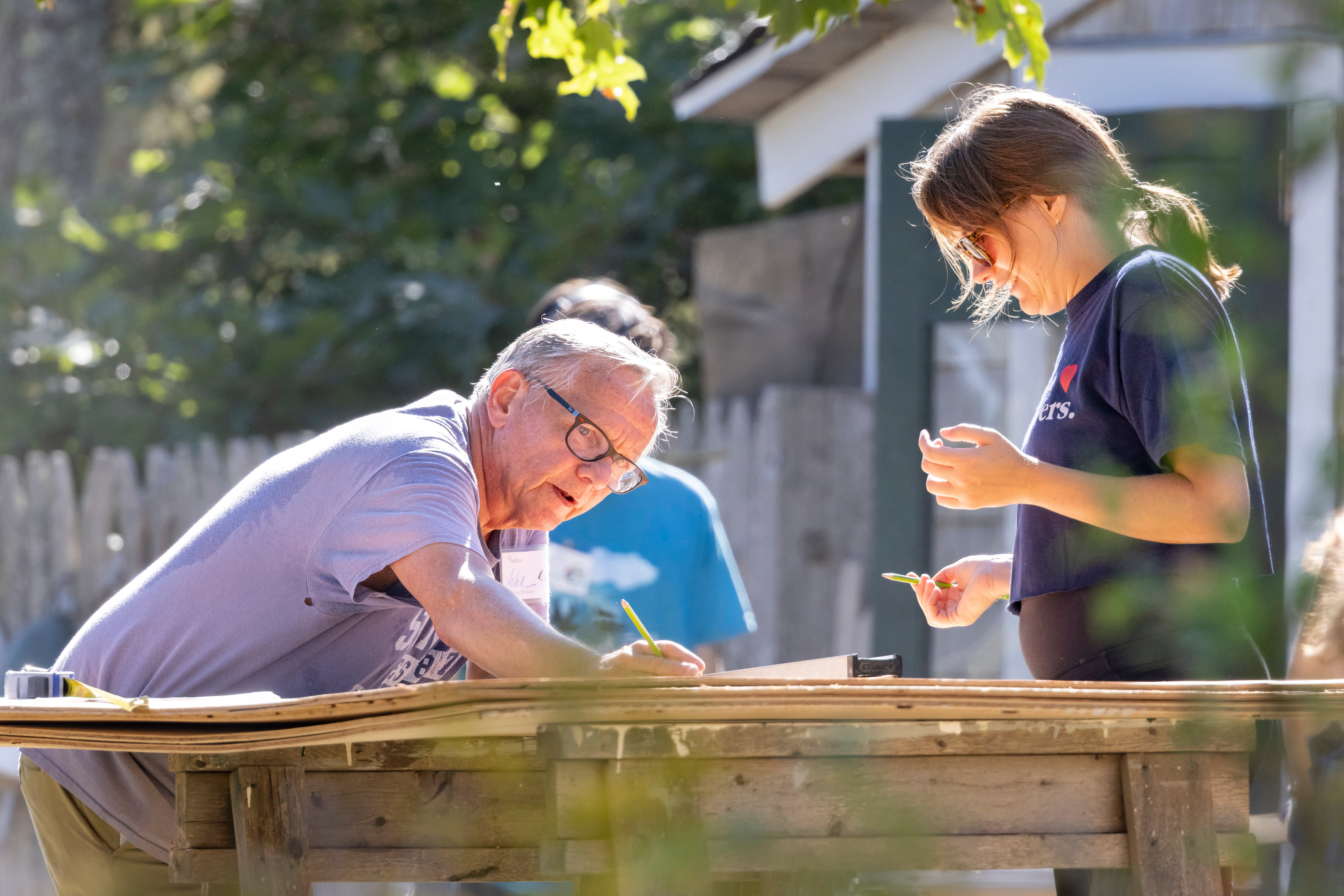 Two people measuring a piece of plywood.