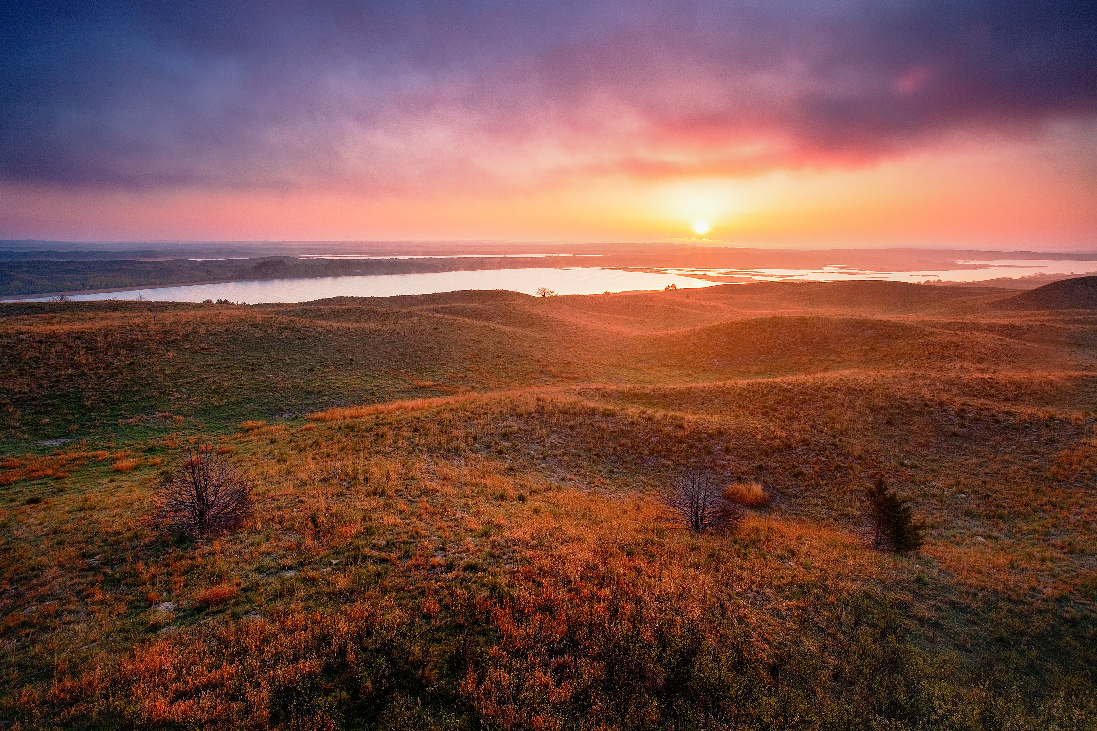 A landscape of expansive prairie and distant lakes under a colorful purple sunrise.