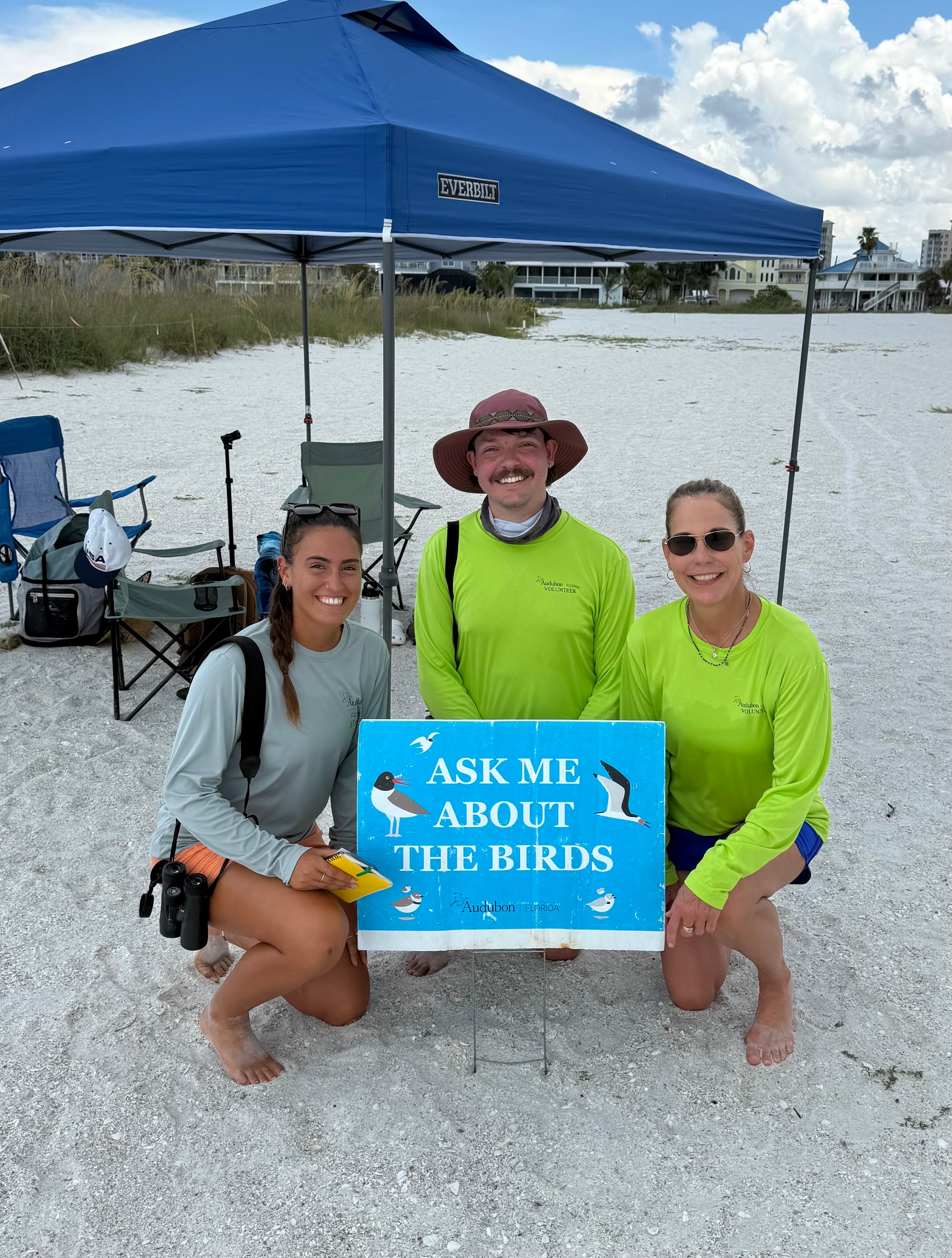 three people in front of an "ask me about the birds" sign