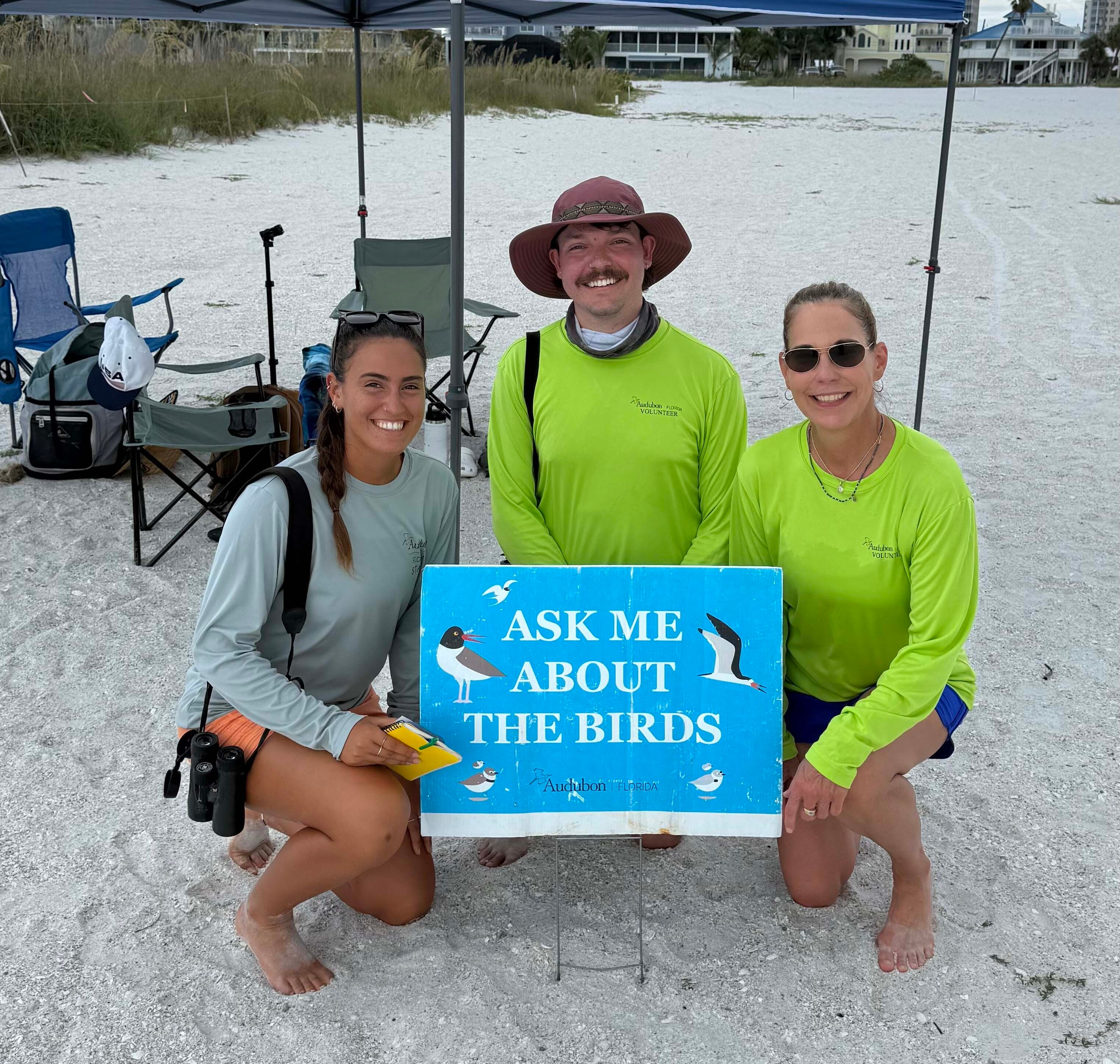 three people in front of an "ask me about the birds" sign