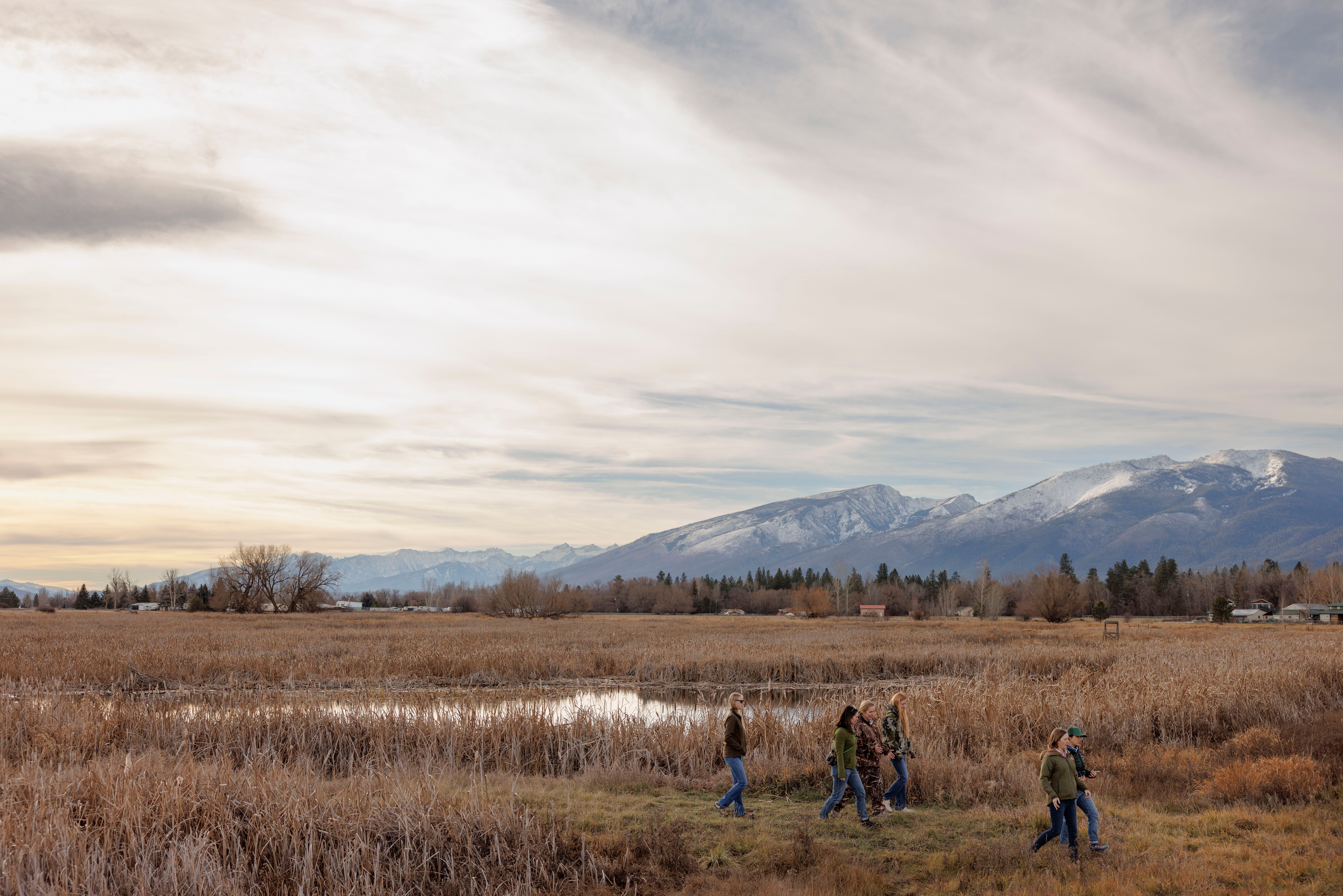 Six people walking through a field at sunset, with mountains in the background.