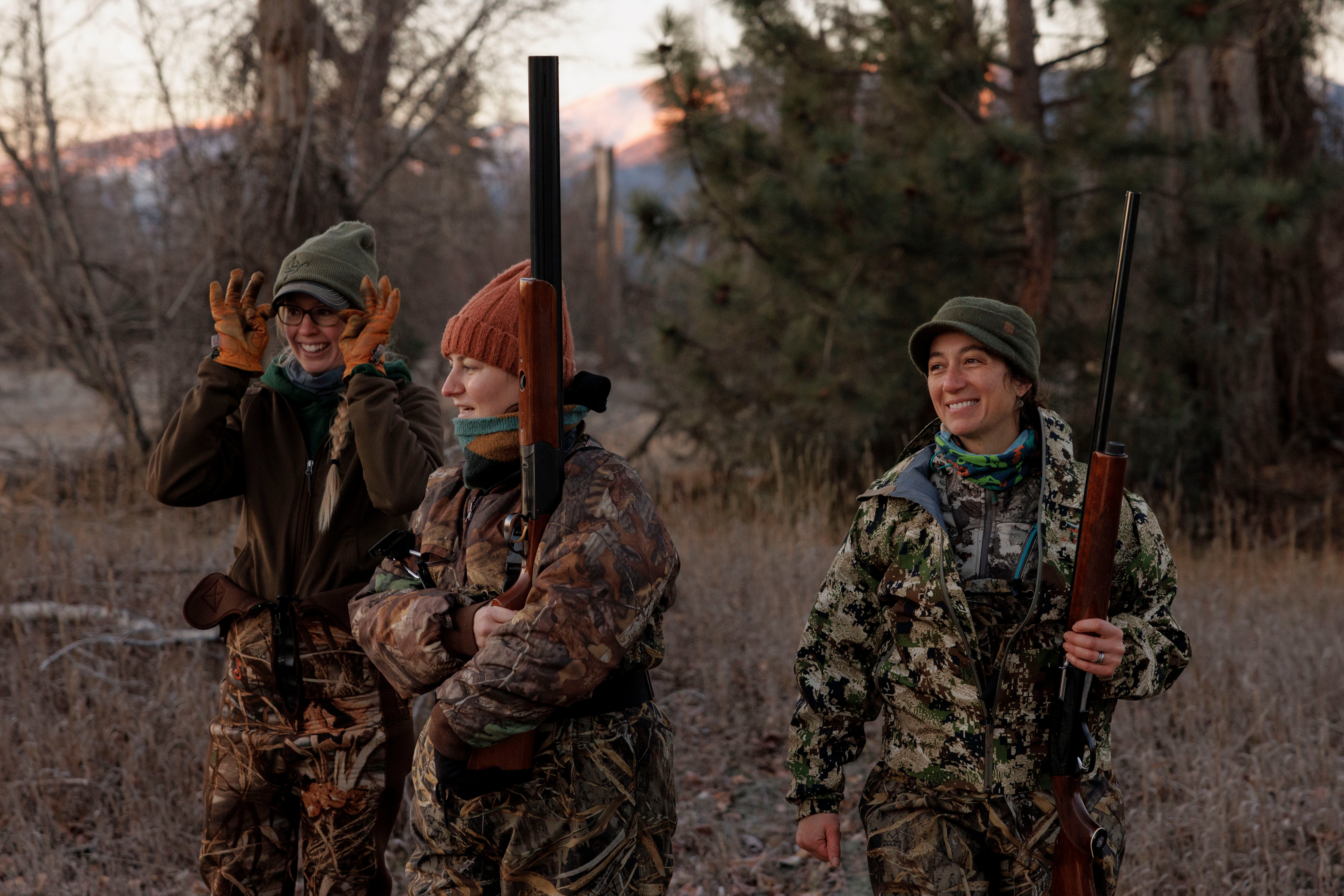 Three women in camouflage clothing holding rifles while laughing and talking.