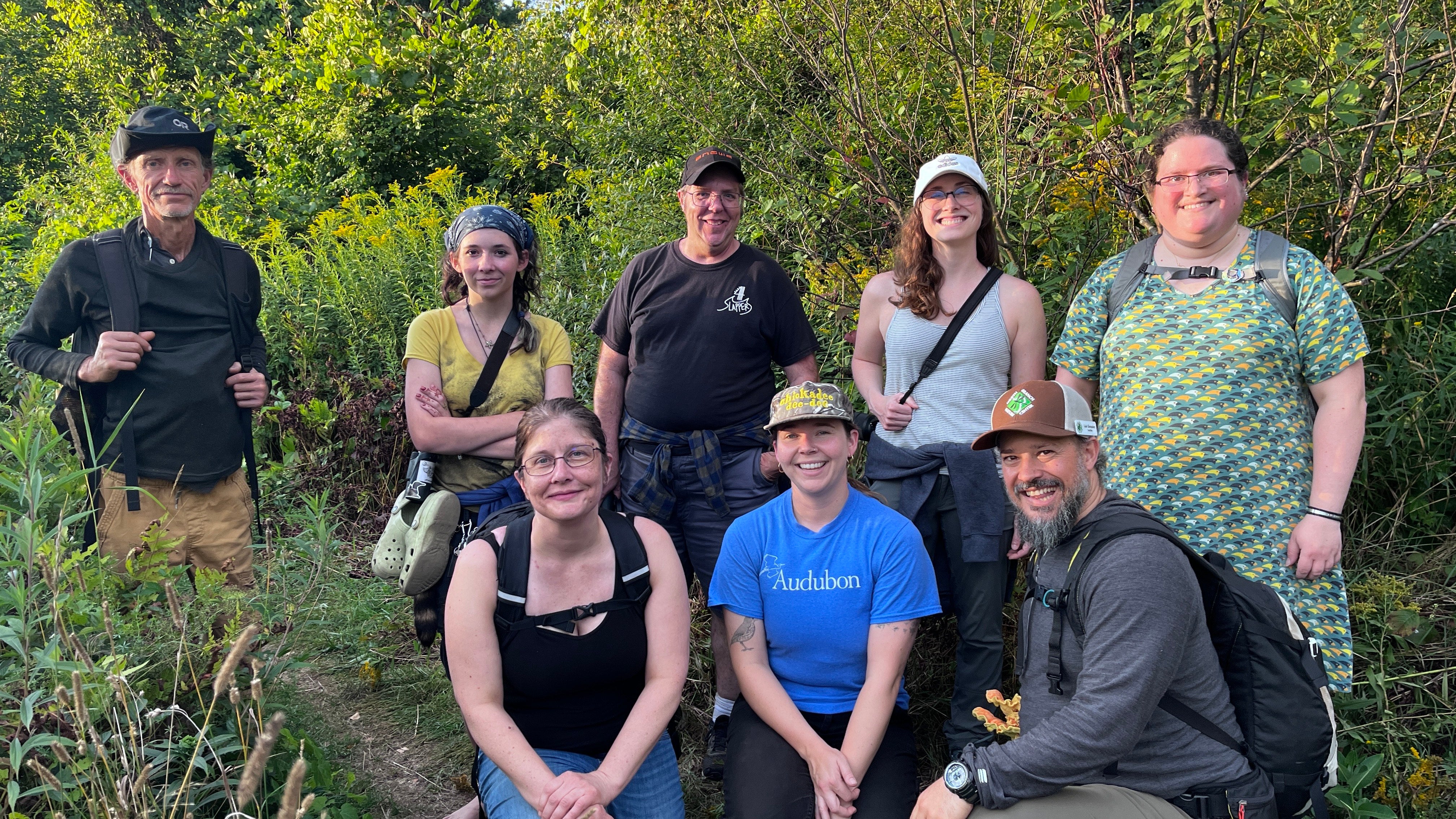 A group of people posing for a group photo on a meadow trail.