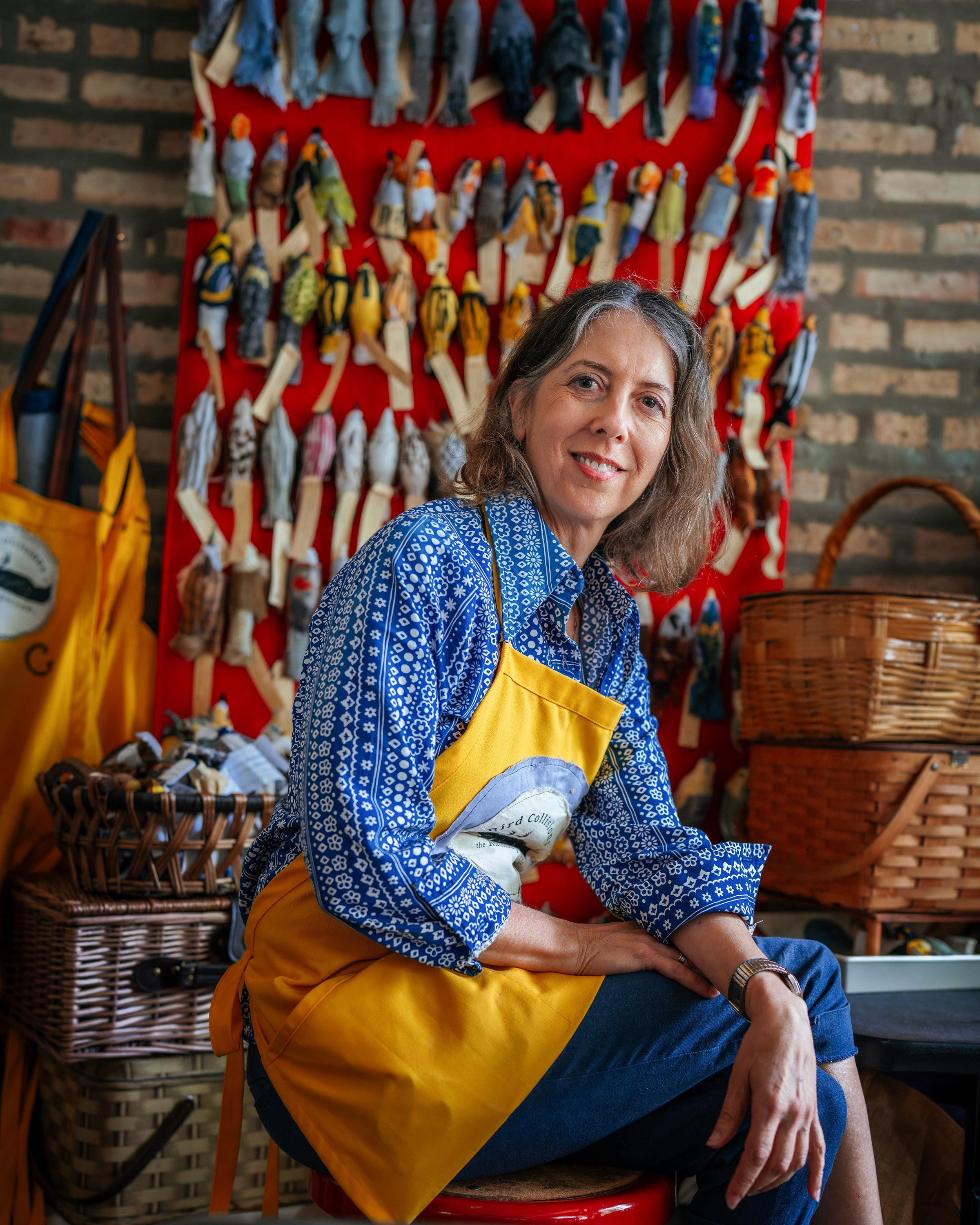Portrait of Holly Greenberg in front of a tapestry of scrap-fabric birds.