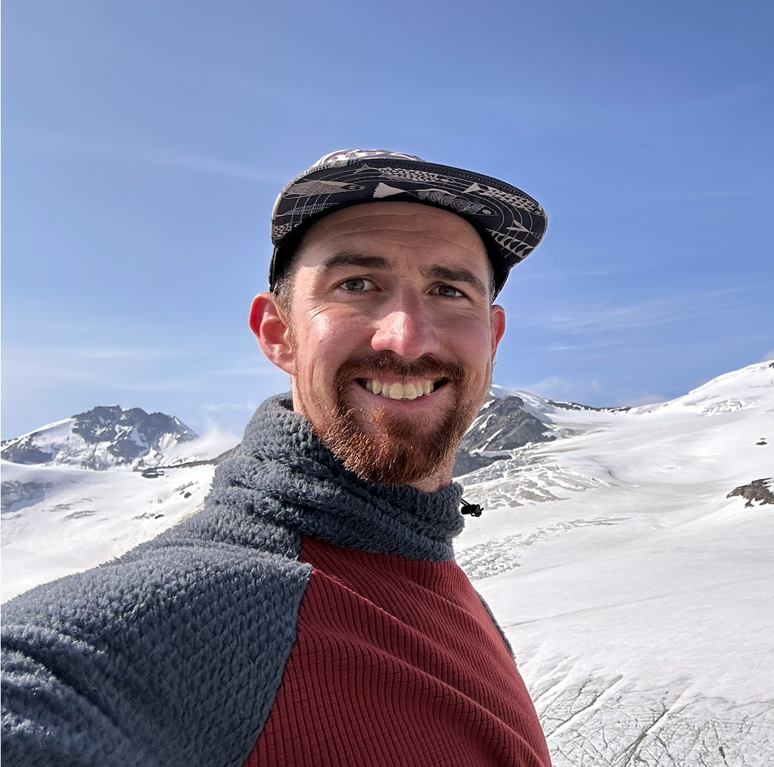A selfie of Caleb Dusek smiling in the mountains covered in snow.