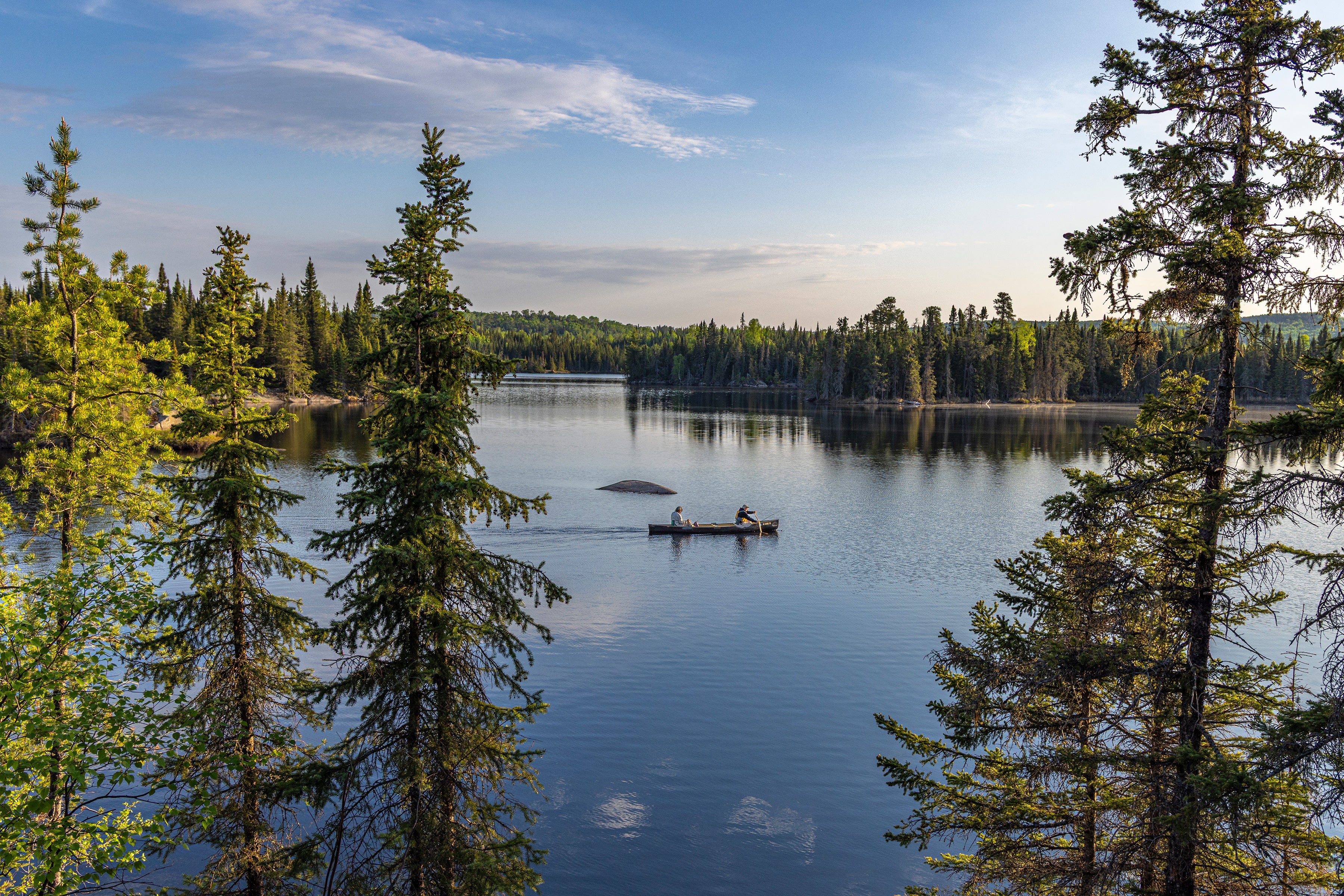 Two people canoe on a pristine lake, lush forest extending into the distance.