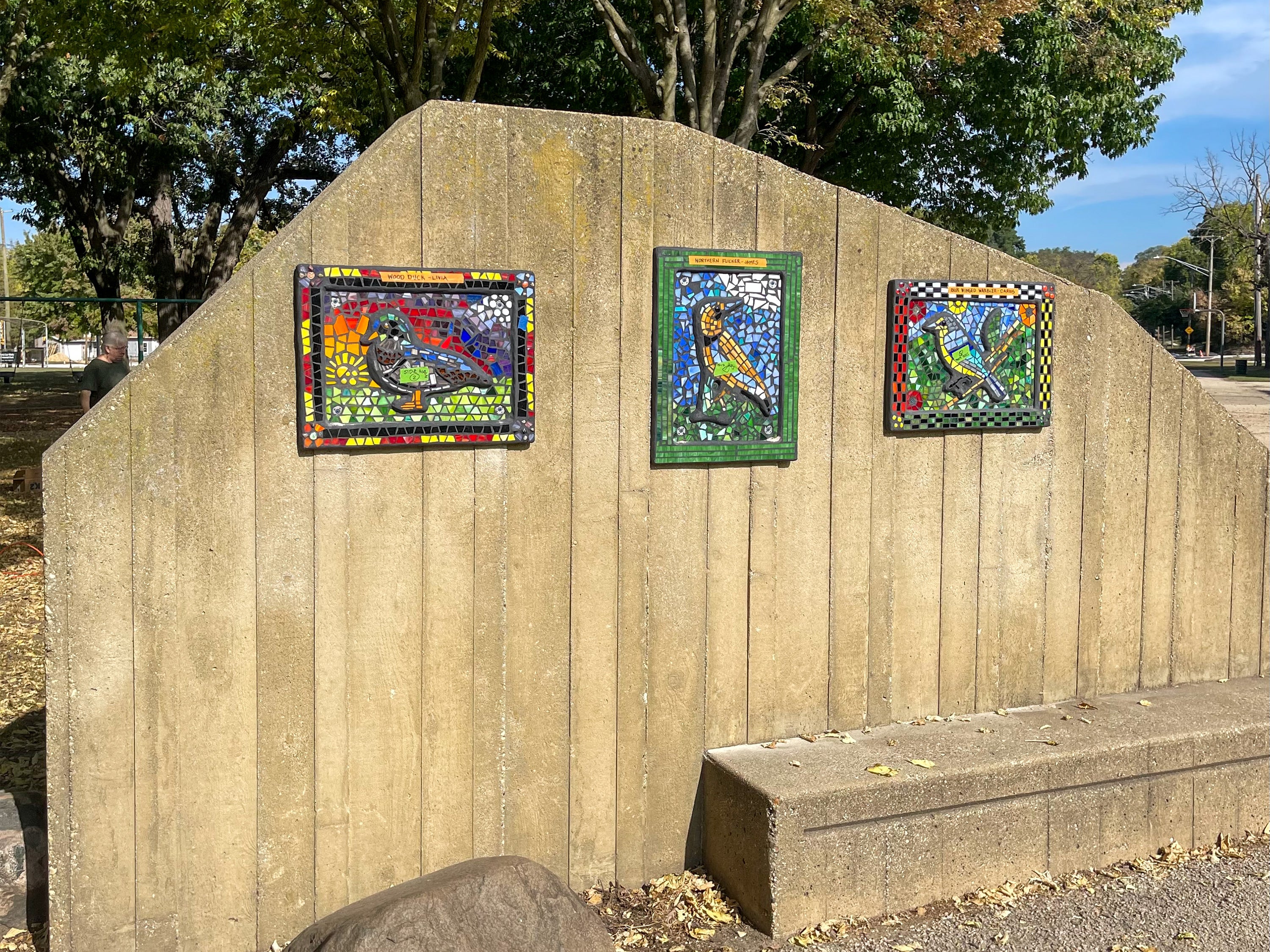 Mosaic art hanging on a fence outside.