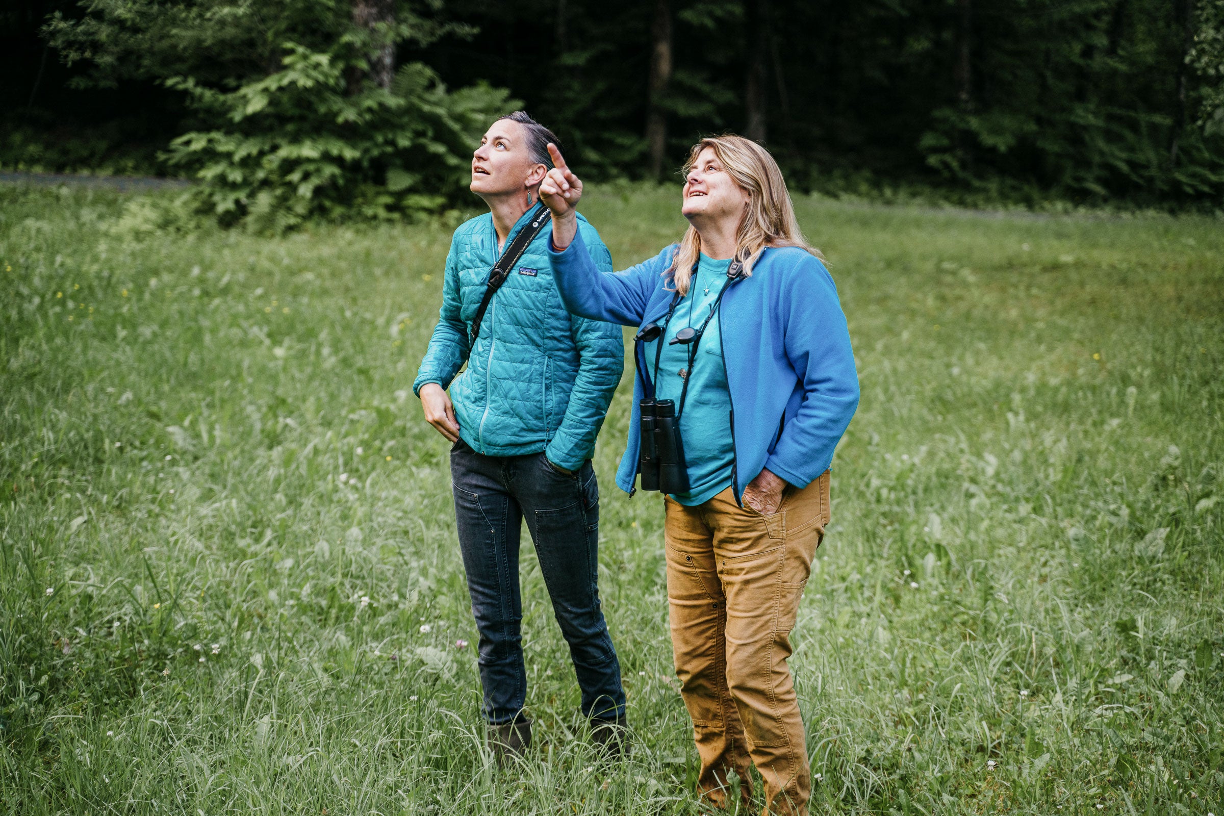 Eliza Minnucci and Jenn Megyesi stand in a field looking up at something Jenn is pointing at.