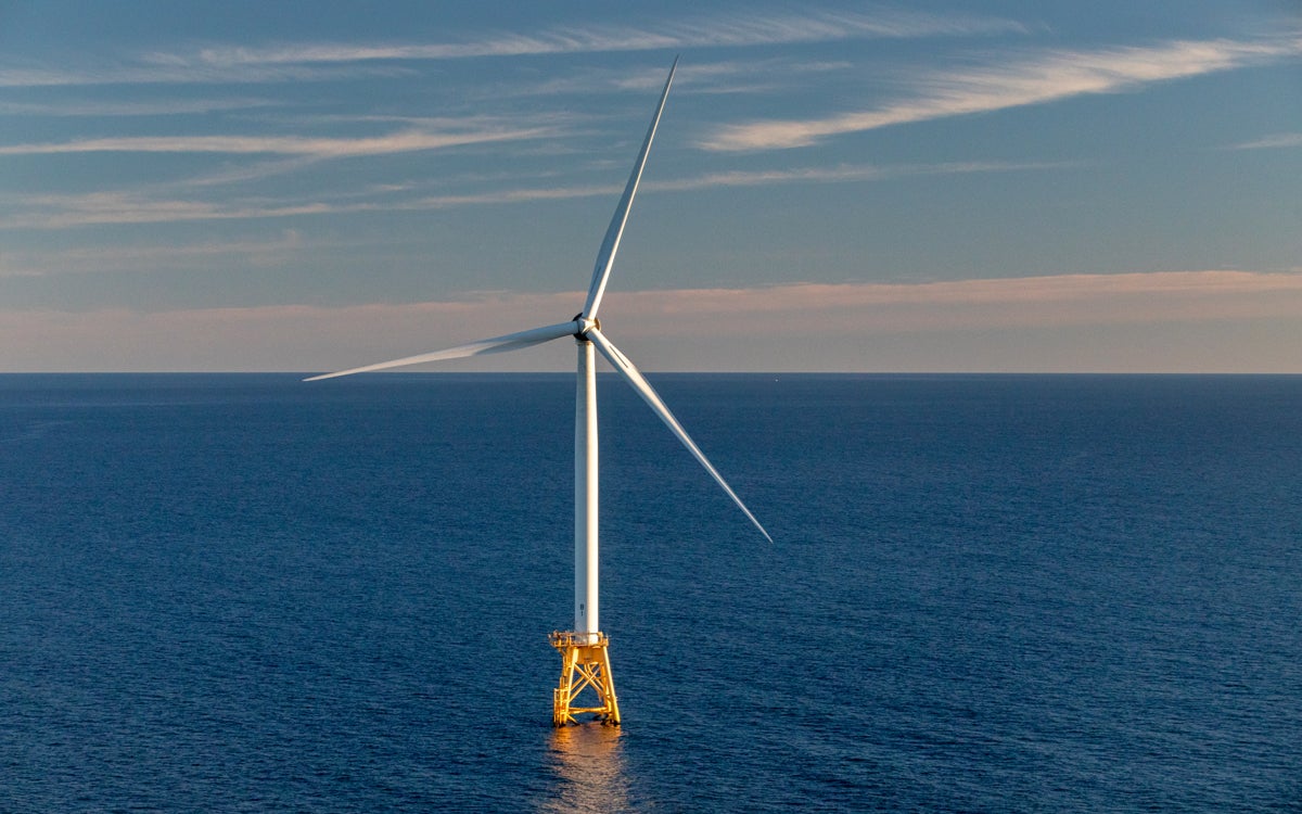 A lone wind turbine is seen in the expanse of blue ocean off the coast of Rhode Island at sunset. 