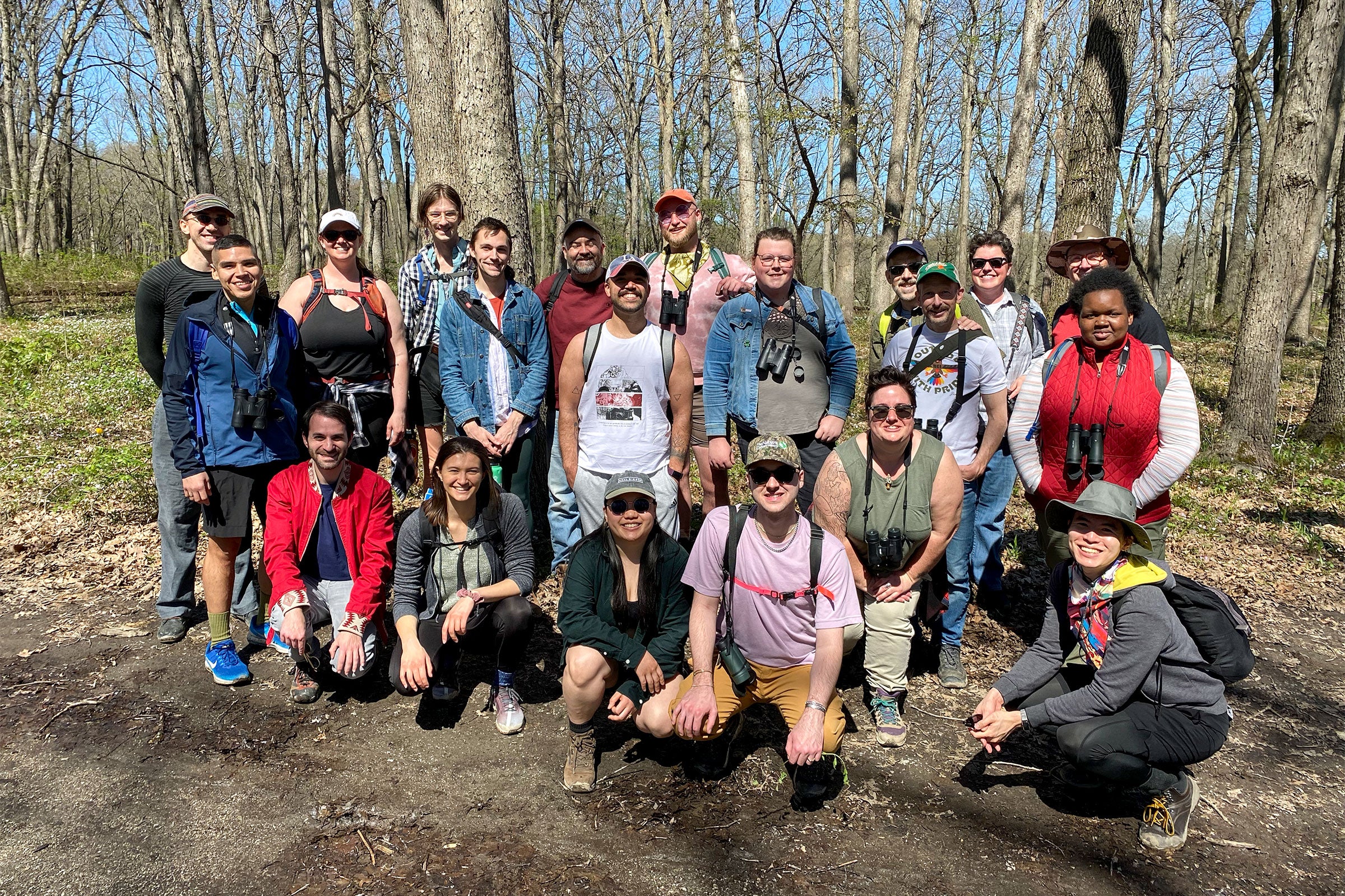 A group of about 30 people stand for a posed photo in a forest—many are wearing hiking and birding gear.