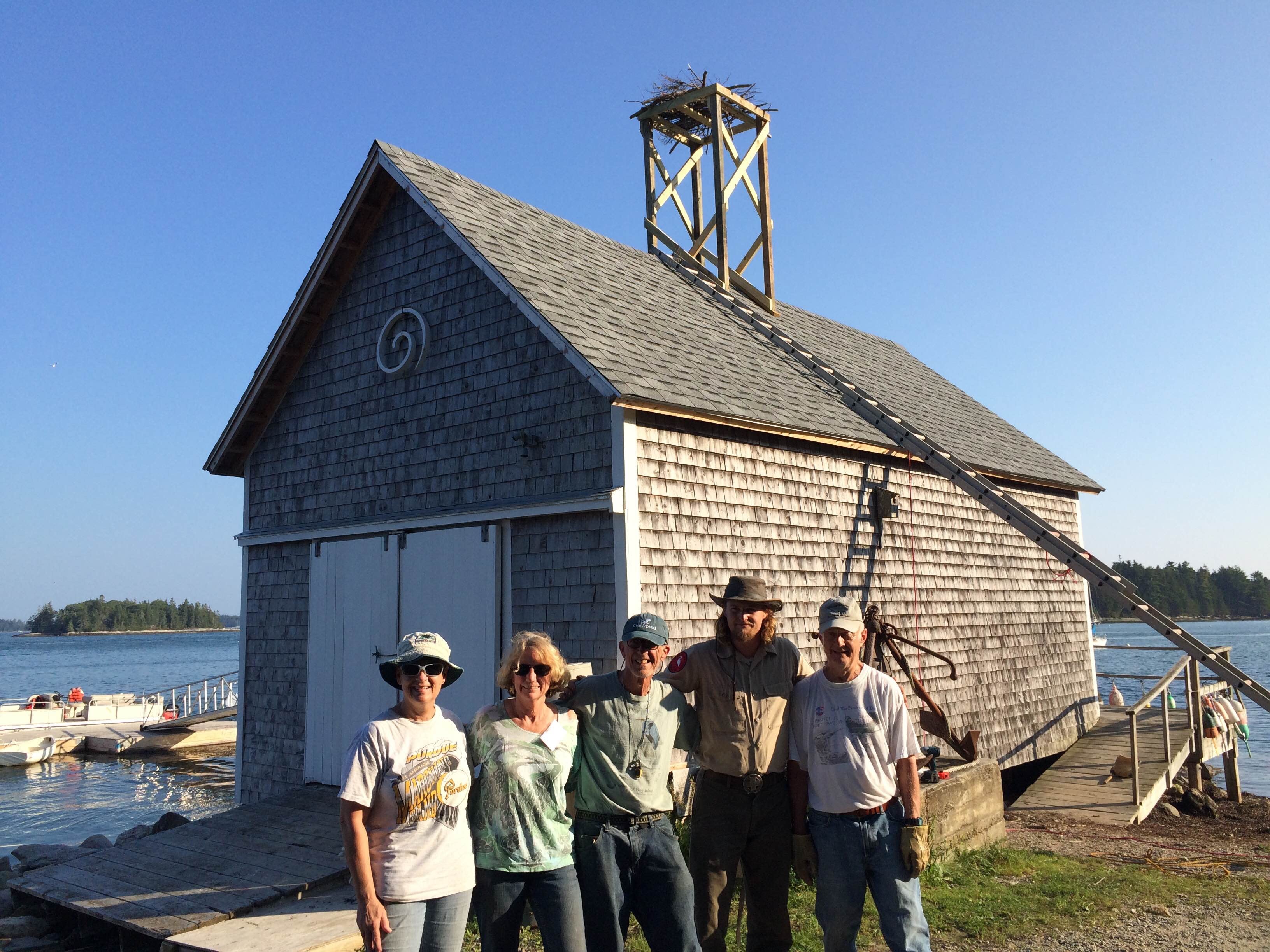Staff and volunteers stand in front of their completed Osprey nest project. Staff and volunteers in front of the mainland Boat House after building the Osprey nest. Photo credit: Eva Lark/Audubon