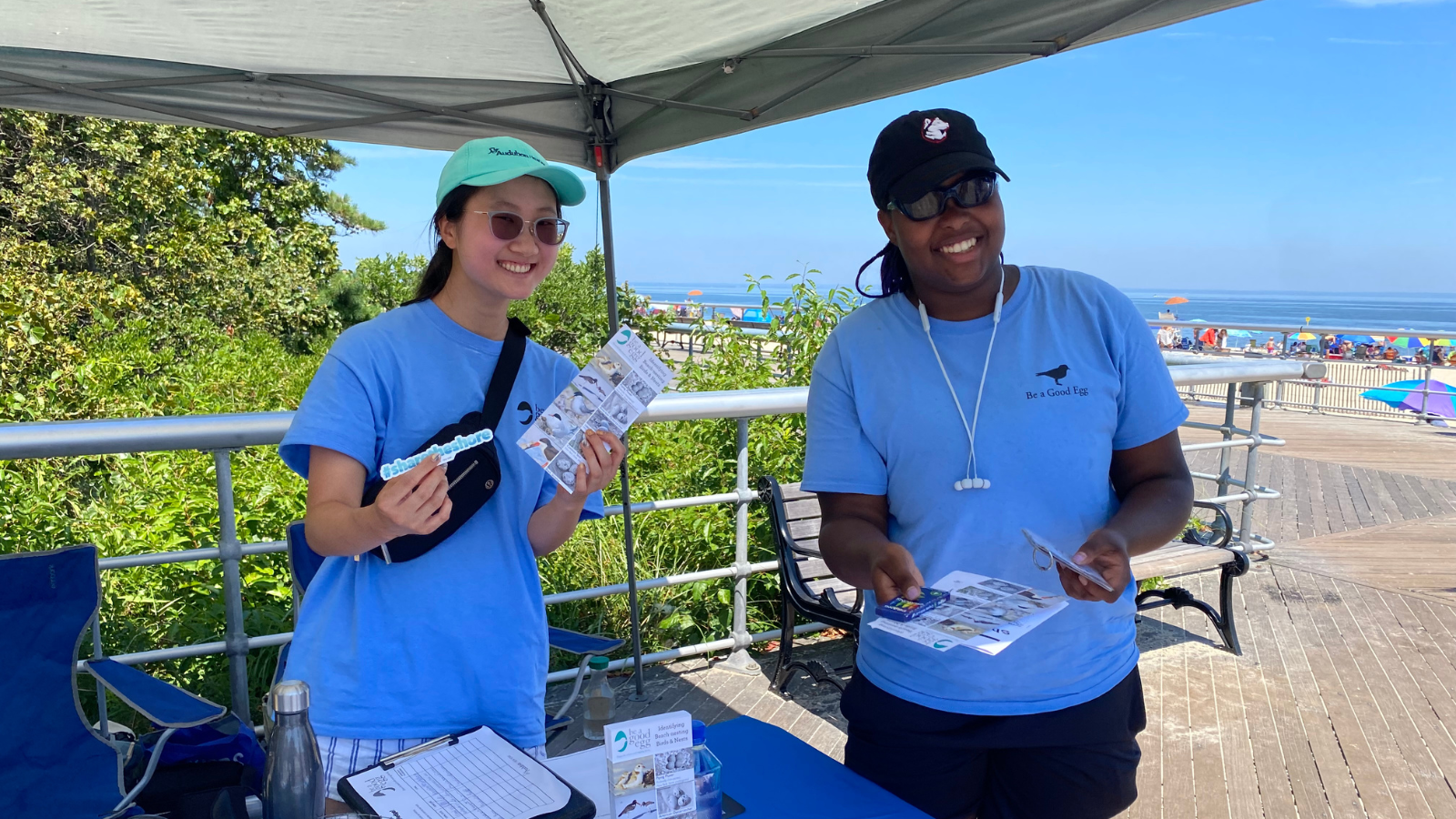 Leila and Kaydence, two young adults, smile and show off Be a Good Egg flyers.
