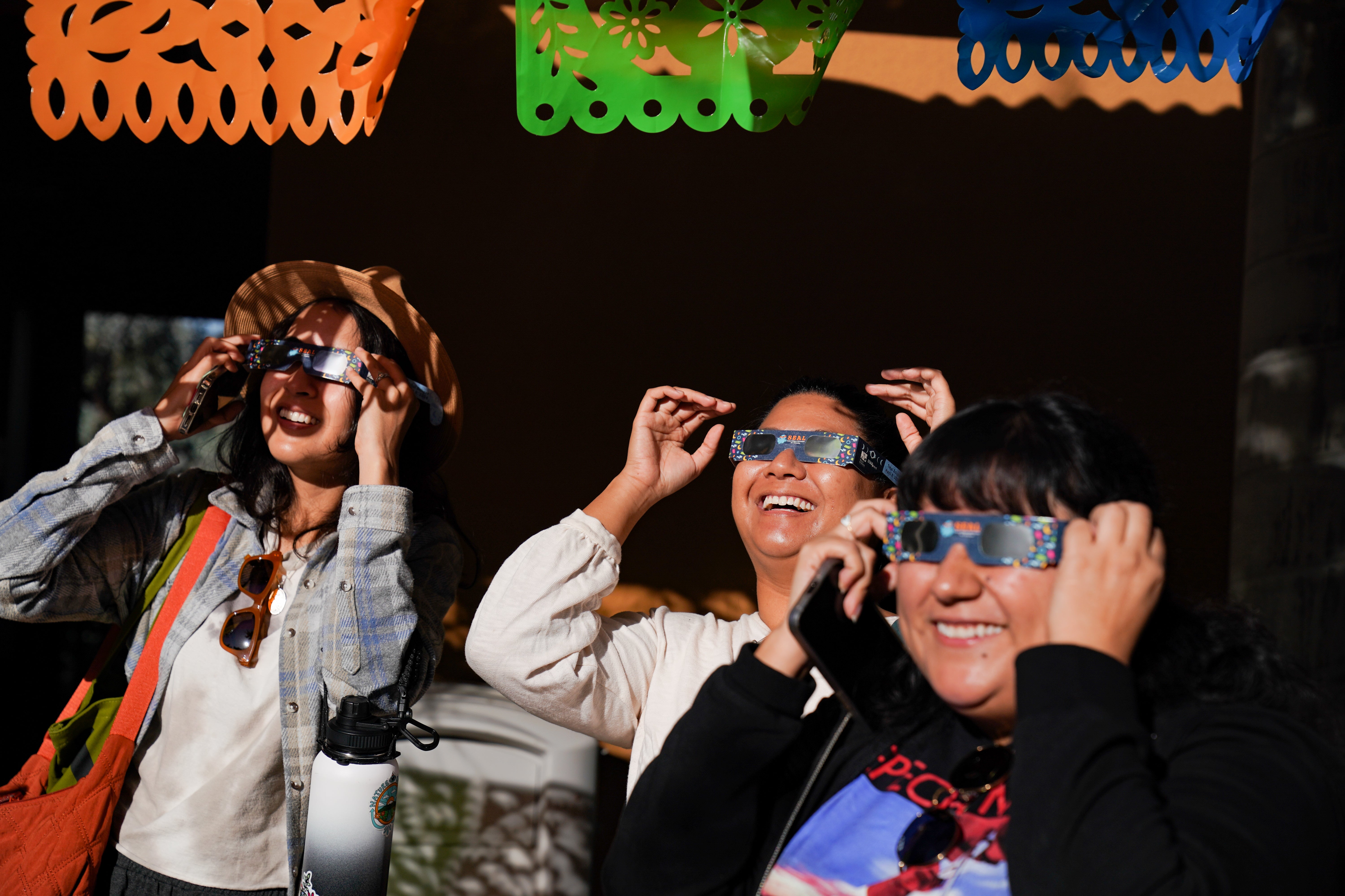 Three adults wearing solar glasses and watching the solar eclipse.