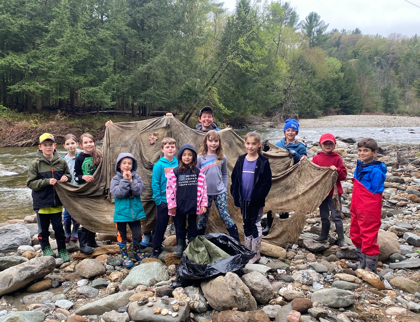 A group of kids poses with trash collected by the river