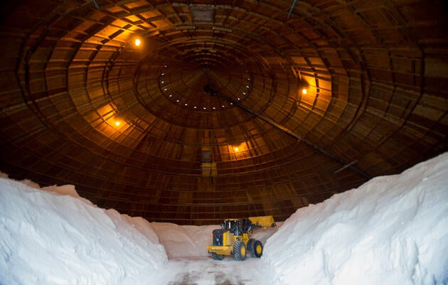 Mounds of stored rock salt minimize a large piece of machinery. 